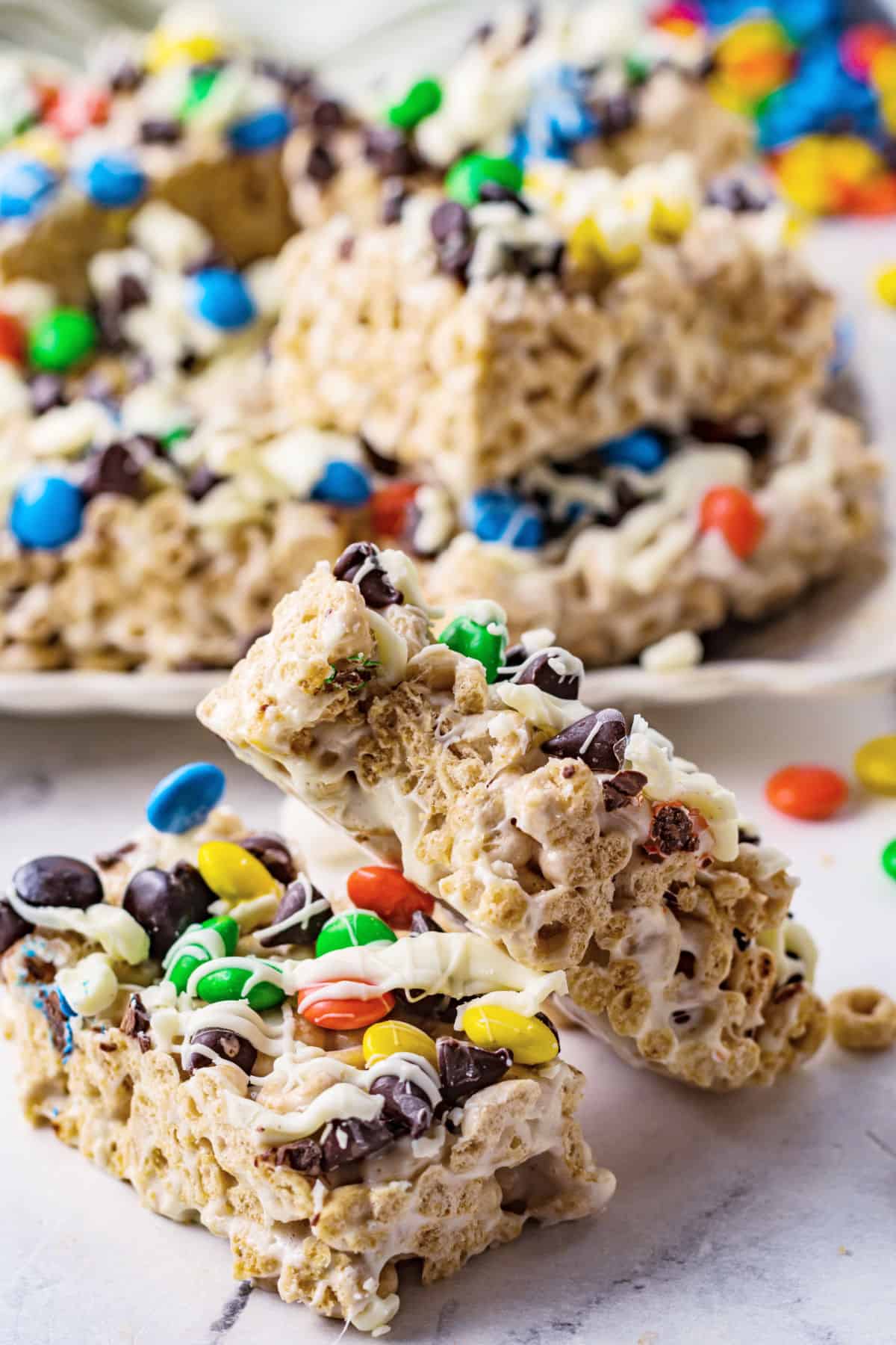 Two no bake cheerio bars with chocolate and M&M's stacked on each other.