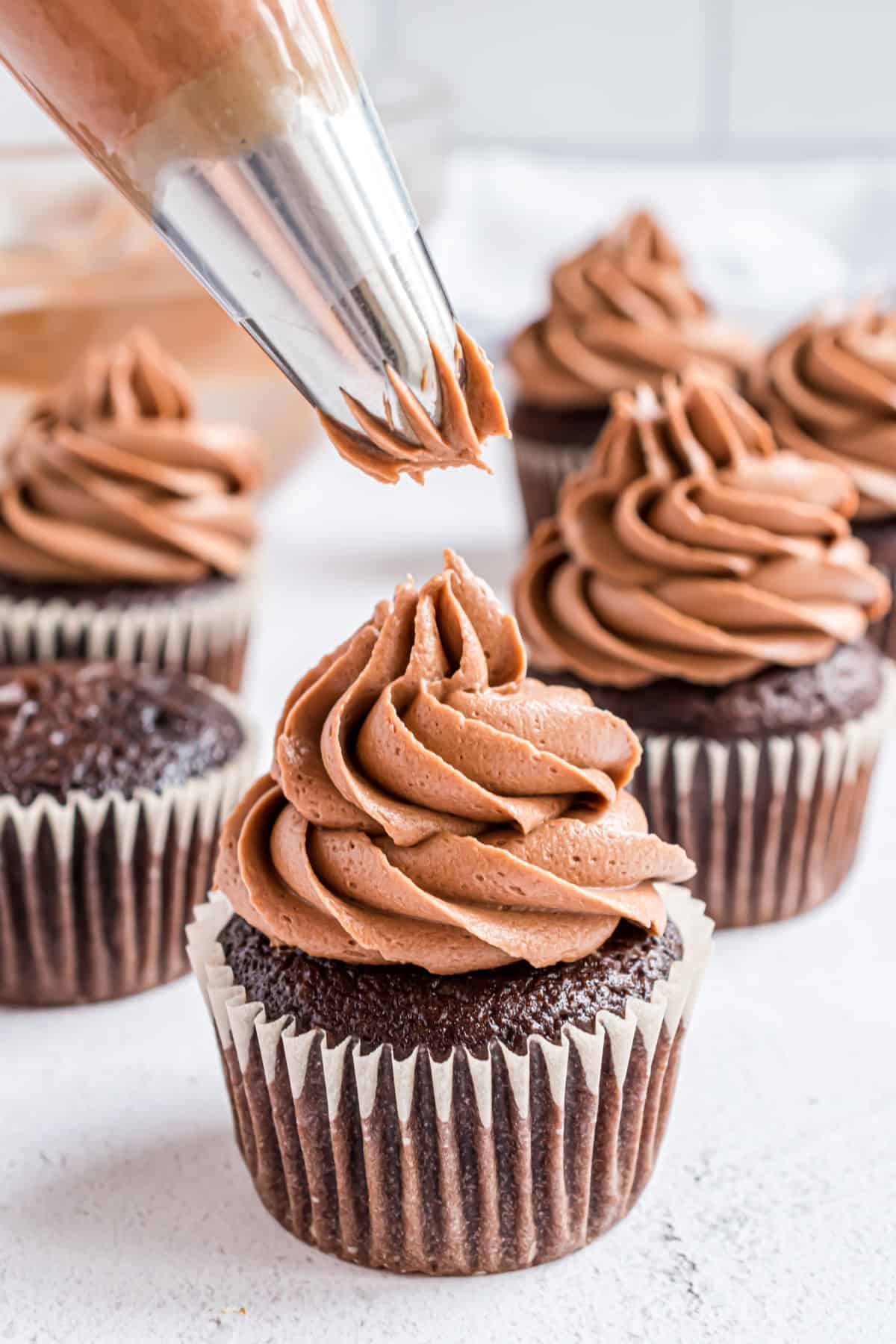 Chocolate cupcakes with chocolate frosting being piped onto them.