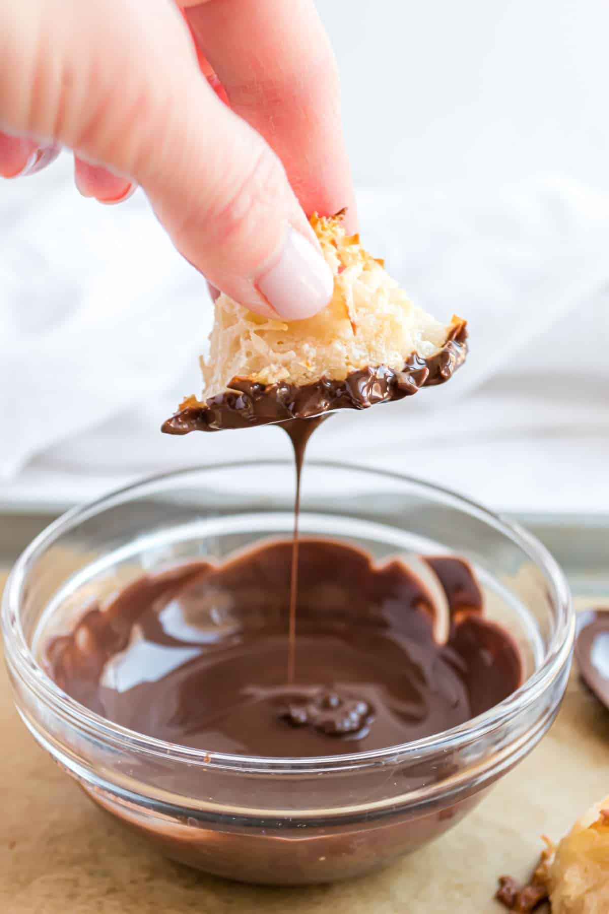 Coconut macaroon being dipped in a bowl of melted chocolate.