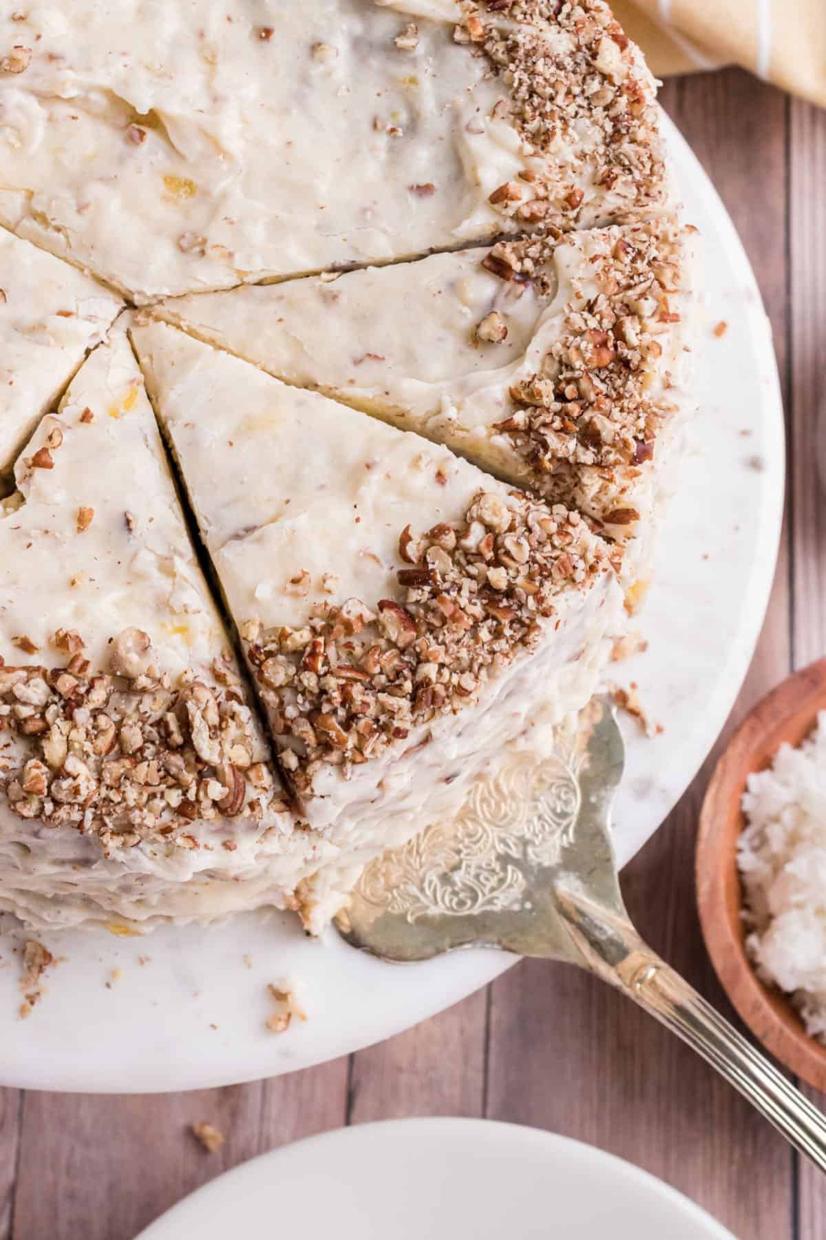 Hummingbird cake with slices made and one being removed from cake platter.