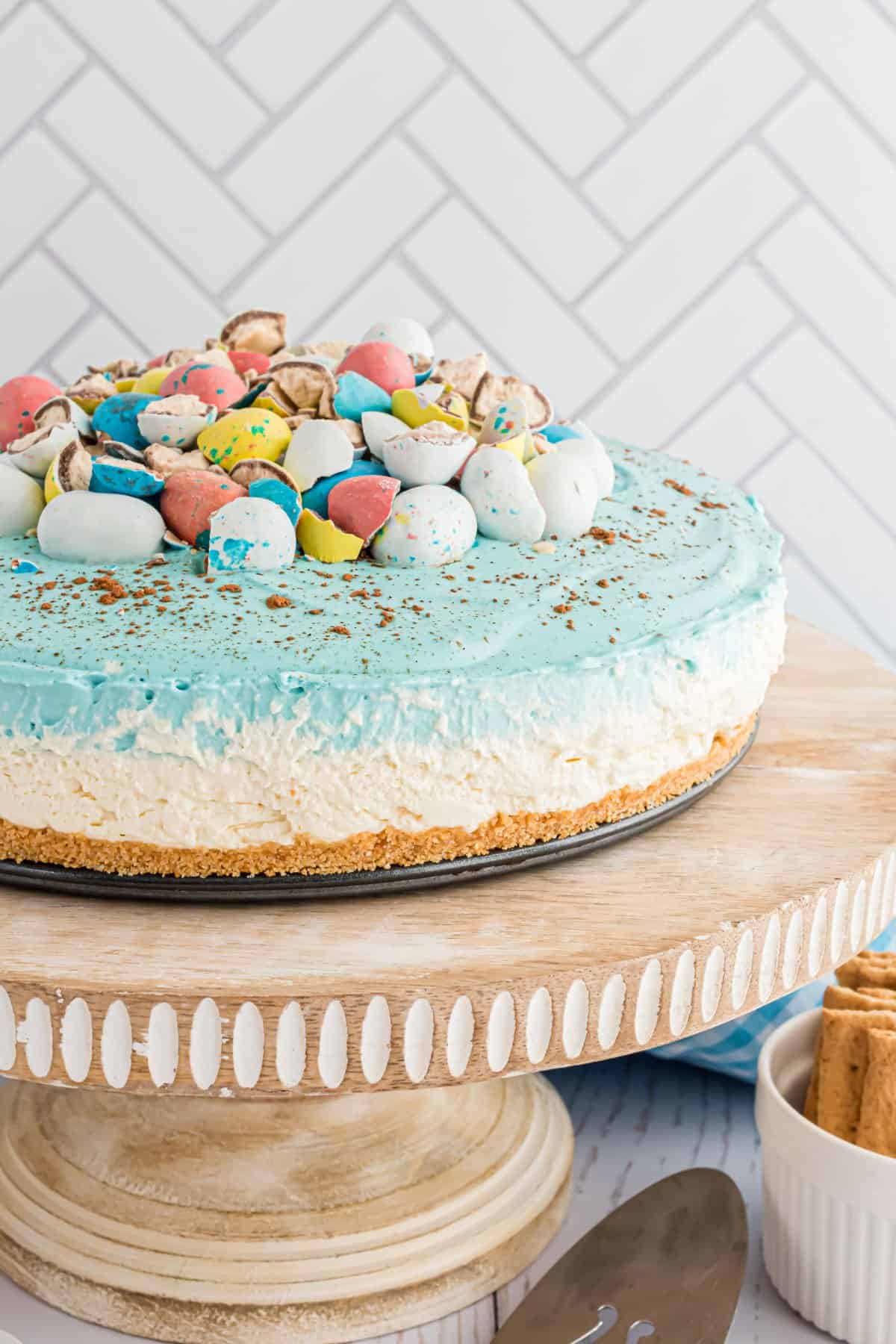 Easter egg cheesecake on a wooden cake server topped with malt balls.