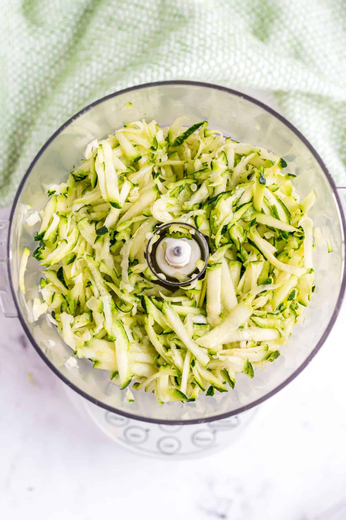 Shredded zucchini in a food processor bowl.