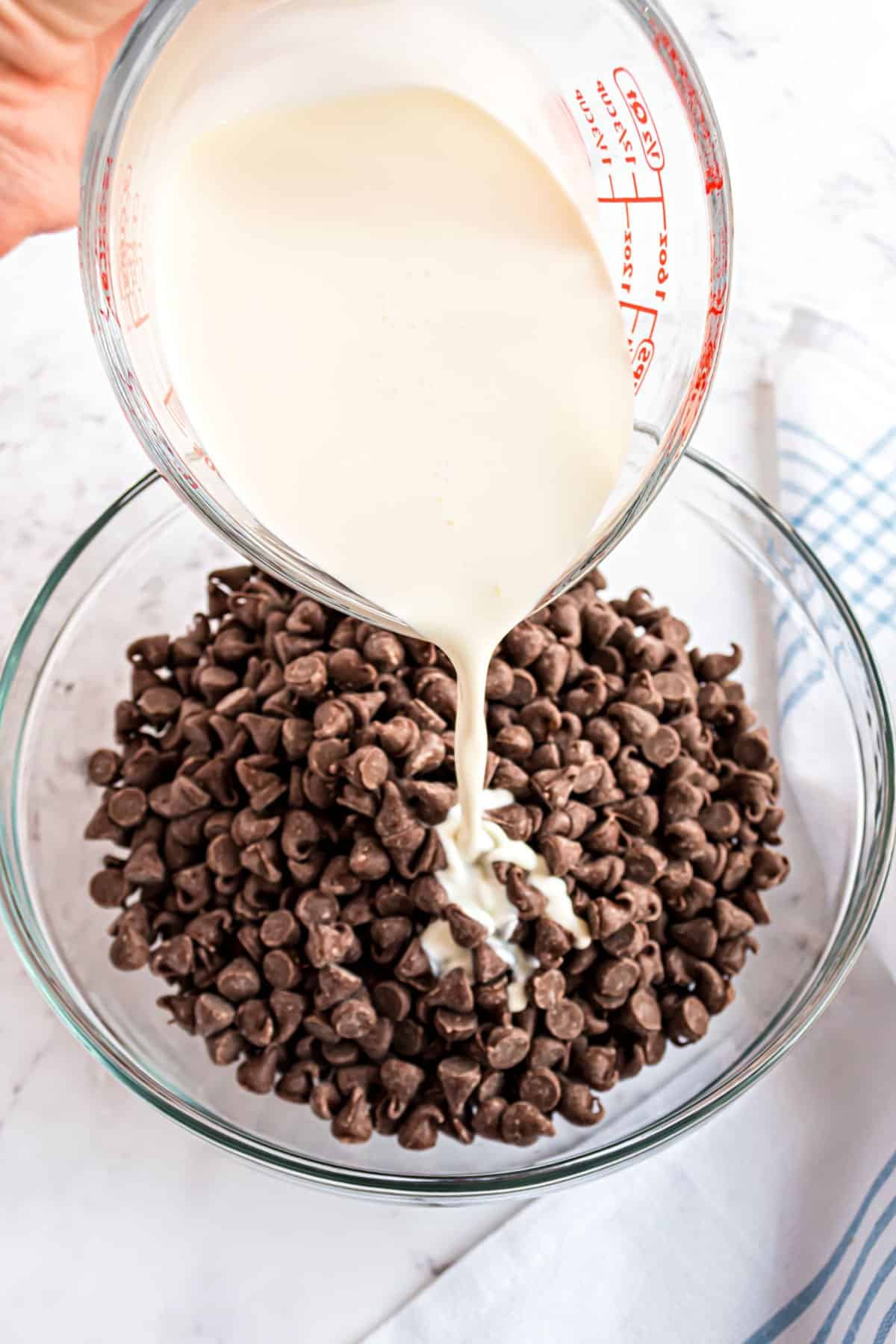 Chocolate chips in a glass bowl with warm cream poured over the top.