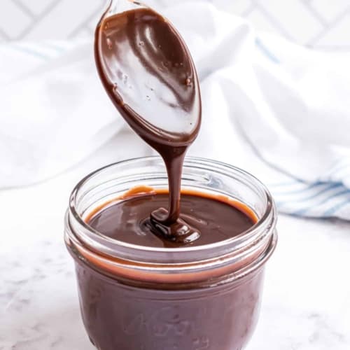 Chocolate ganache in a clear glass jar with a spoon dipped in chocolate.