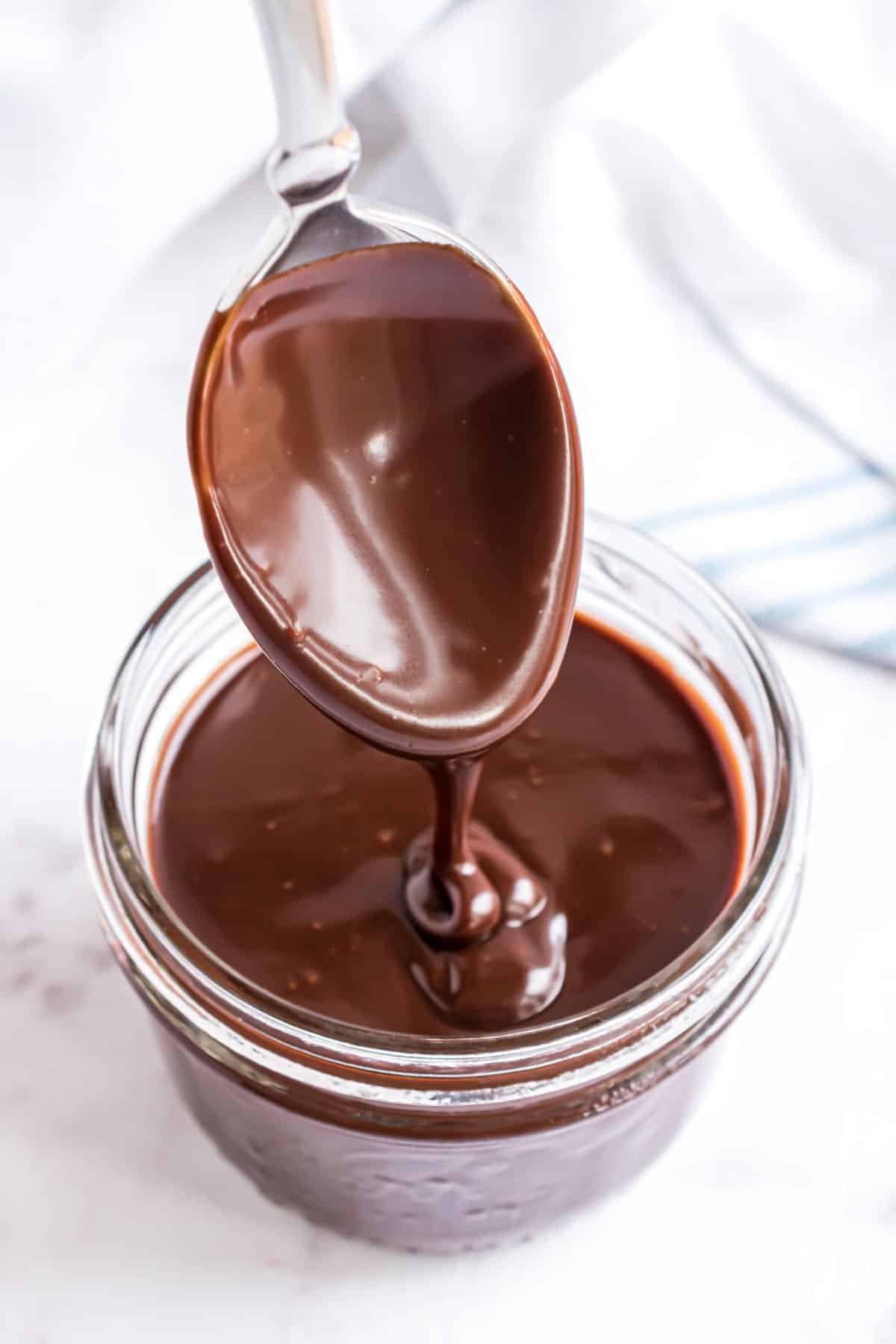 Clear glass jar with spoon dipped in chocolate ganache.