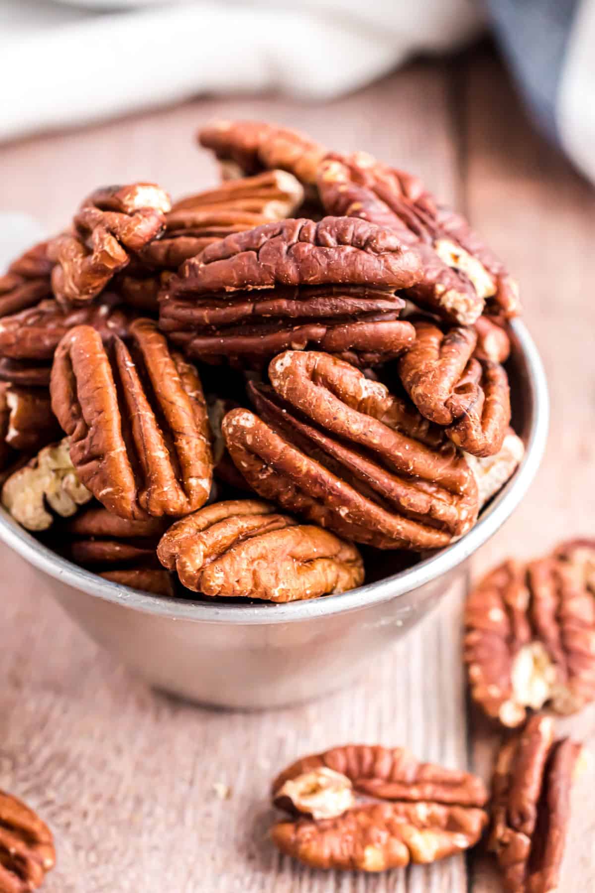 Toasted pecans in a silver measuring cup.
