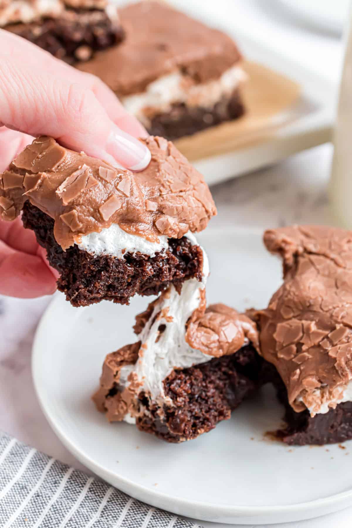 Chocolate brownie with marshmallow being broken in half on a plate.