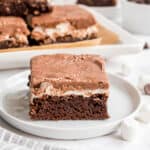 Slice of brownie with marshmallow and chocolate icing on a white plate.