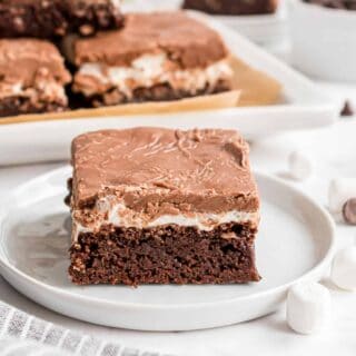 Slice of brownie with marshmallow and chocolate icing on a white plate.