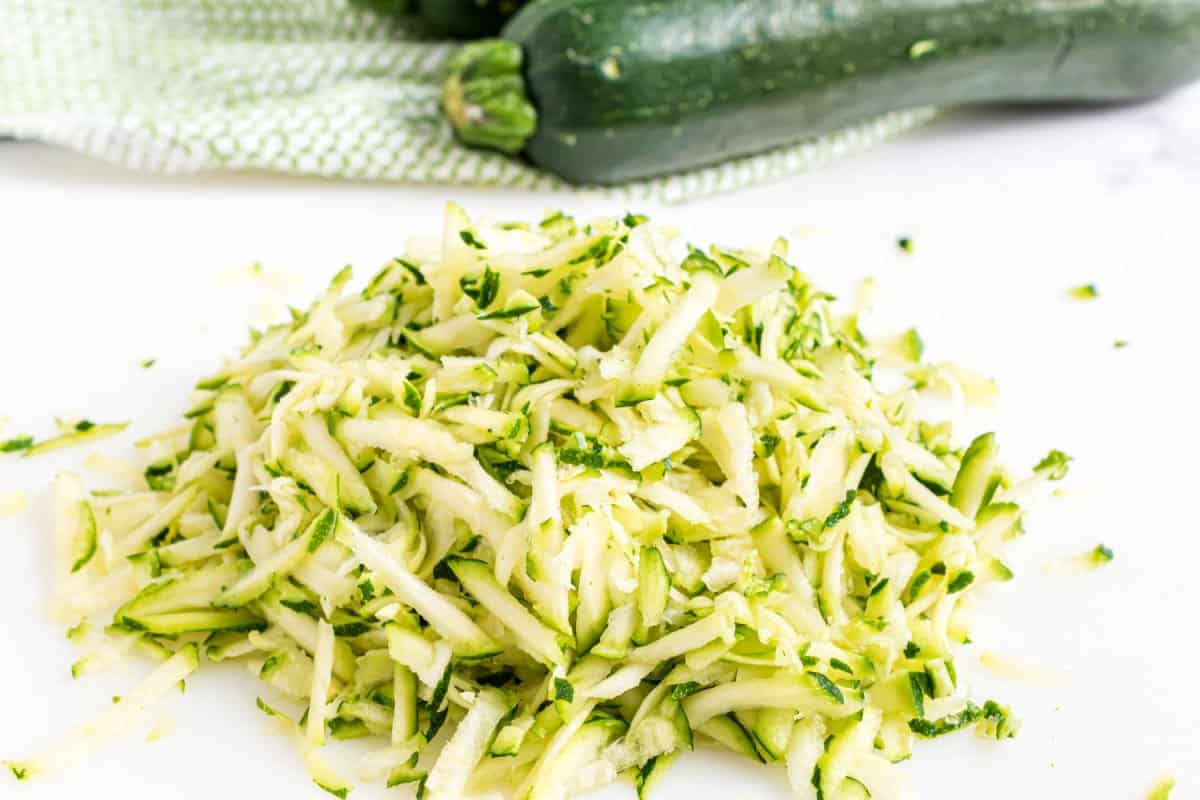 Shredded zucchini on white cutting board.