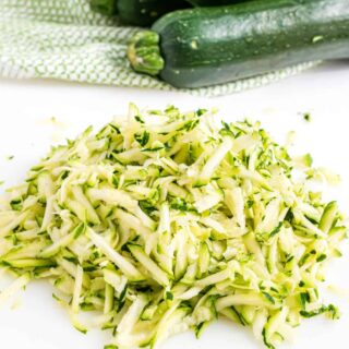 Shredded zucchini with skin on white cutting board.