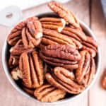 Toasted pecans in silver measuring cup.