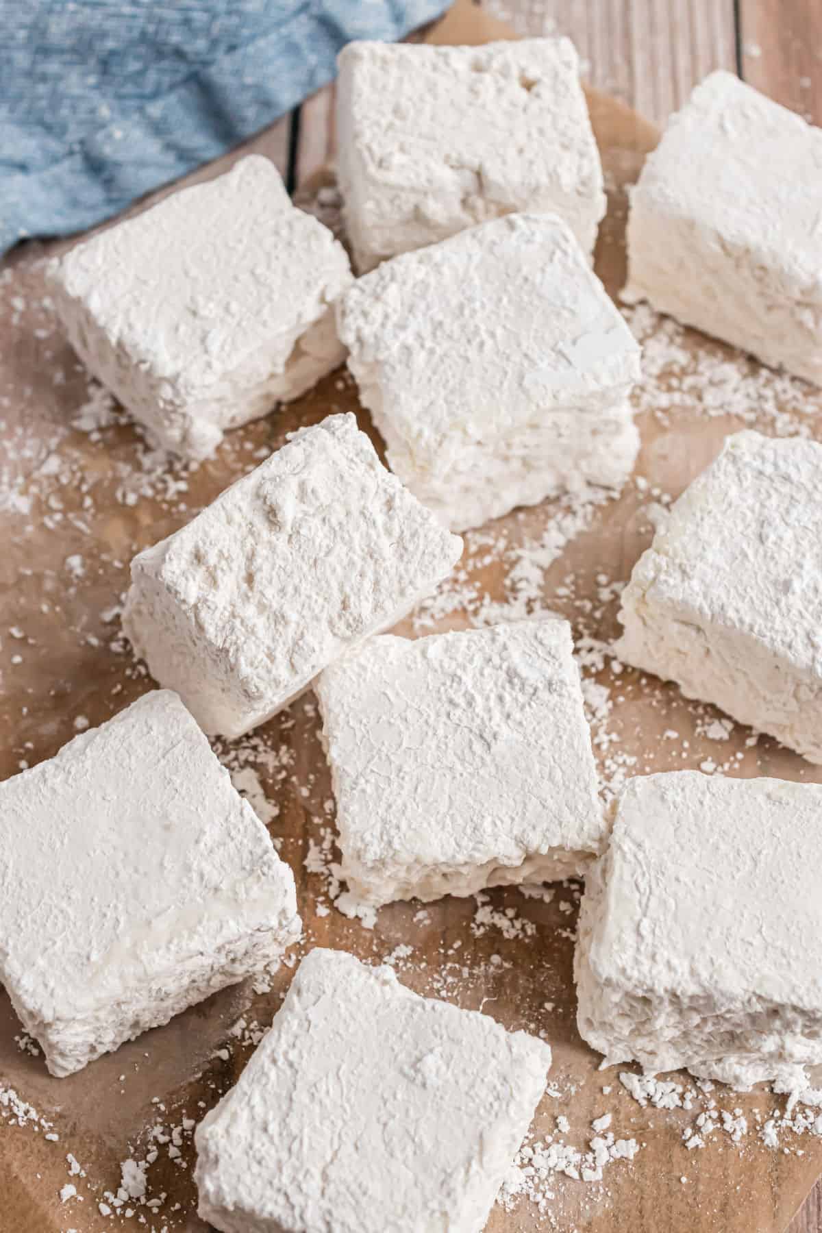 Homeade marshmallows cut into squares on wooden cutting board.