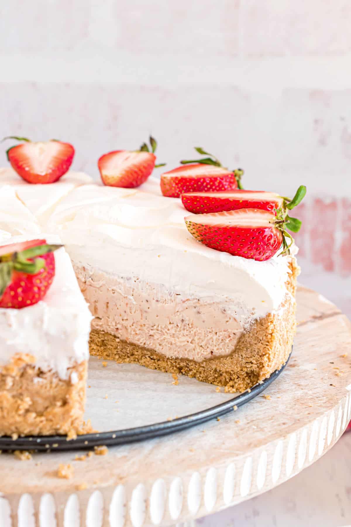 Whole strawberry cheesecake on cake platter with one slice removed.