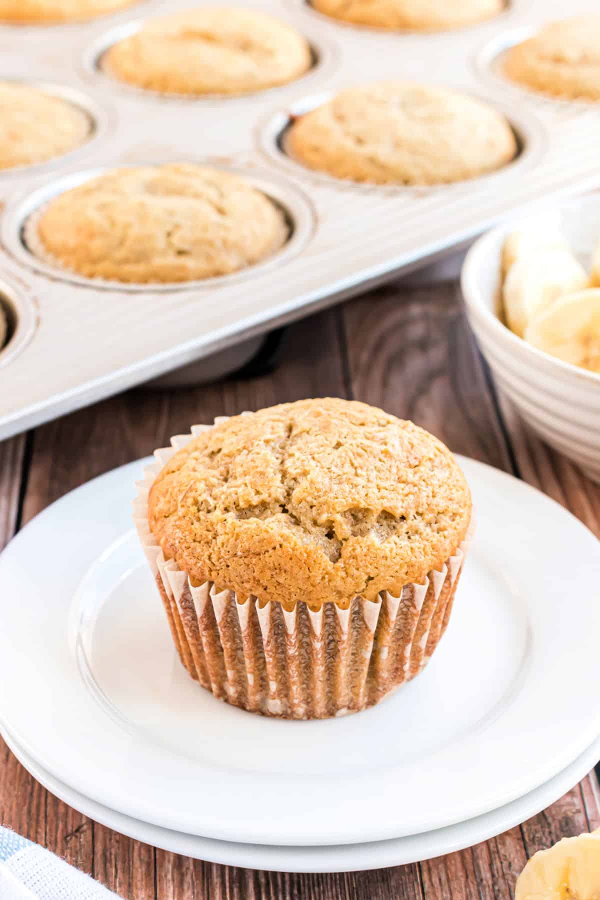 Banana bread muffins in cupcake tin with one on a plate.