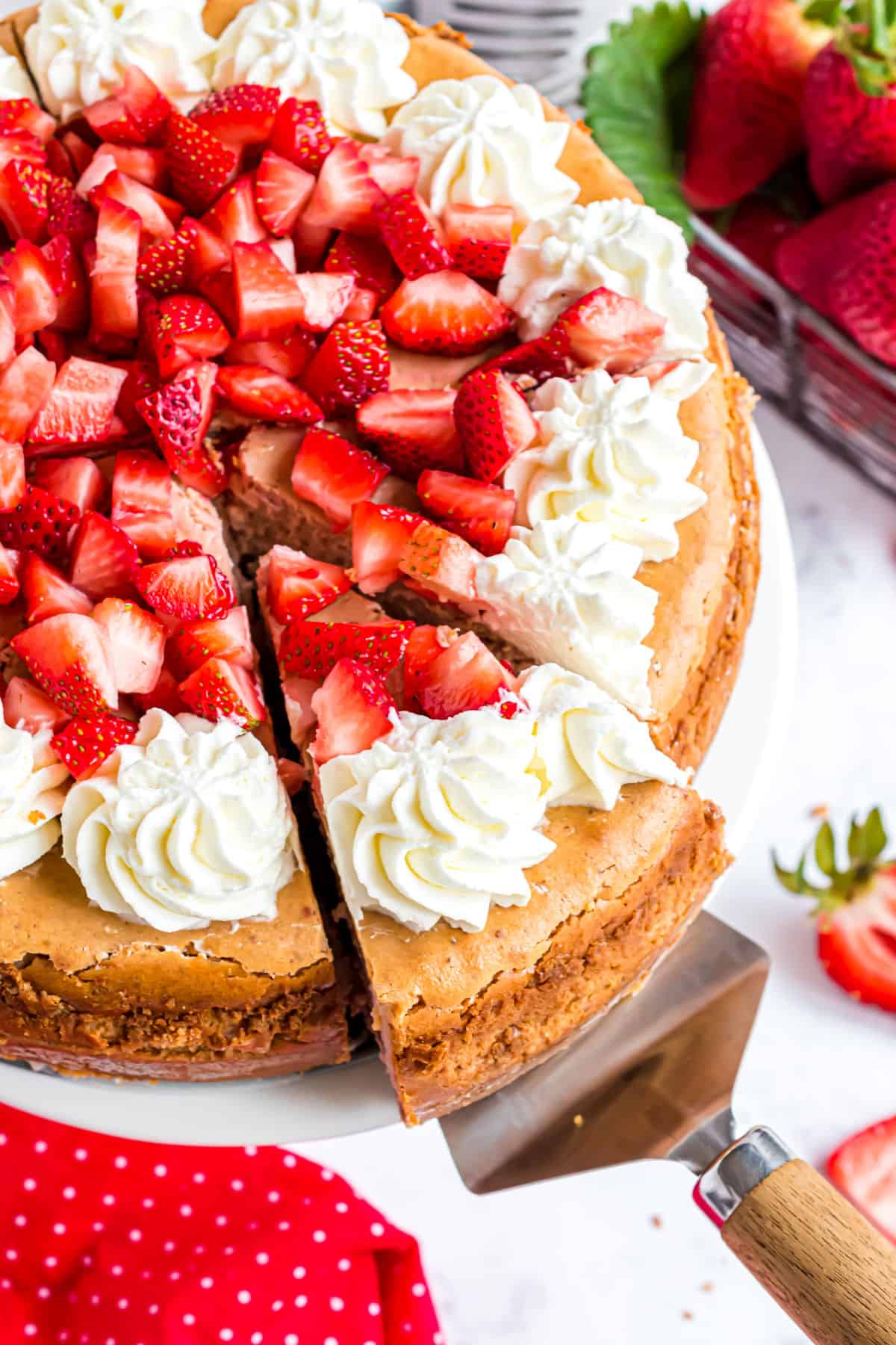 Strawberry cheesecake topped with fresh berries and whipped cream with a slice being removed.