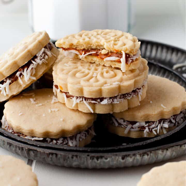 Alfajores cookies stacked on a black plate.