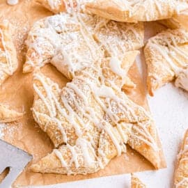 Cheese filled danish with powdered sugar and vanilla glaze on parchment paper.