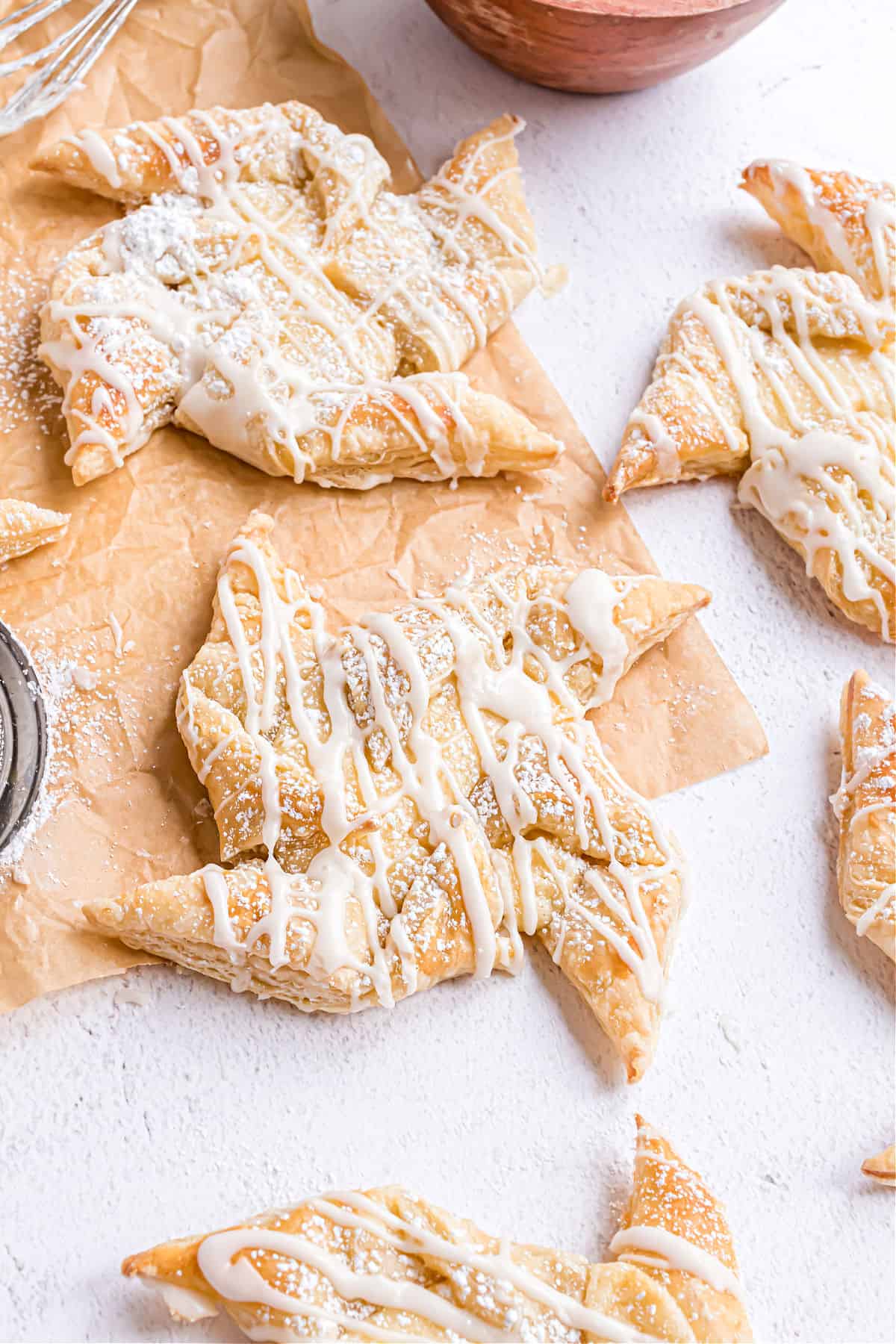 Cheese danish on parchment paper with vanilla icing and powdered sugar.