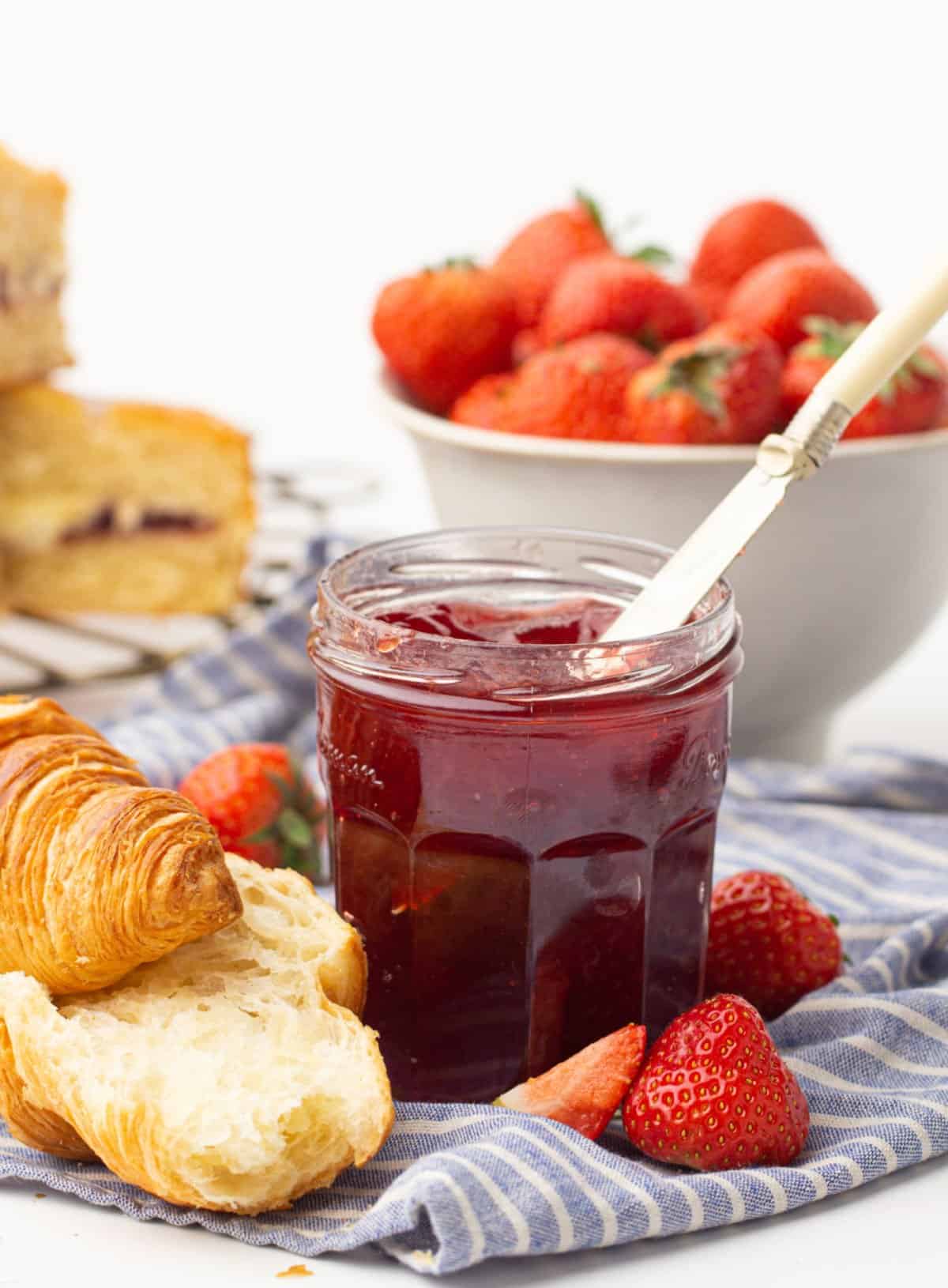 Strawberry jam in a jar with croissants.