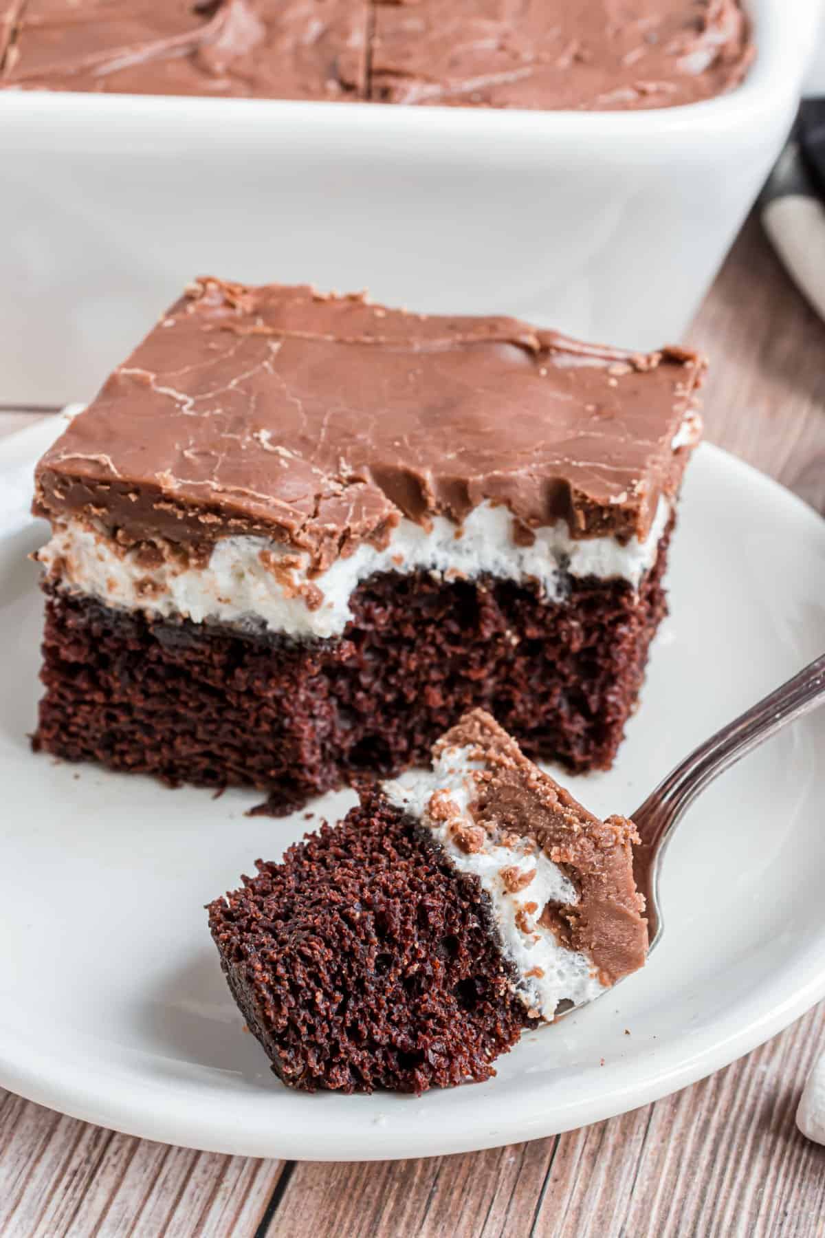 Slice of chocolate cake with marshmallow and chocolate frosting on a white plate.