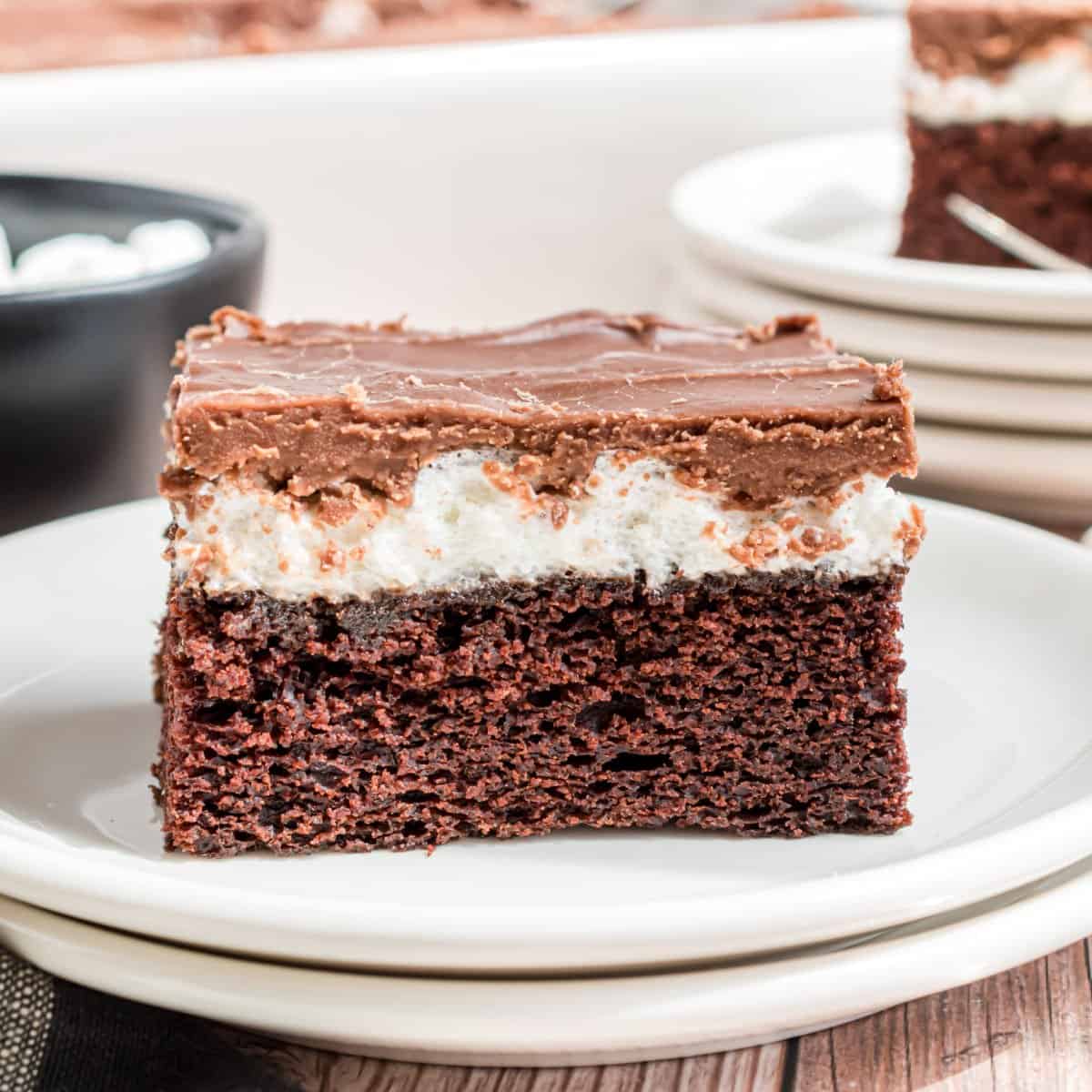 Slice of chocolate cake layered with melted marshmallow and fudgy frosting on a stack of white plates.