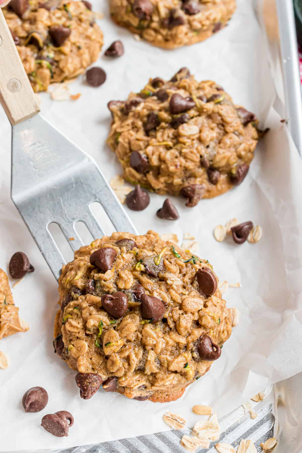 Chocolate chip oatmeal zucchini cookies on parchment paper lifted with spatula.