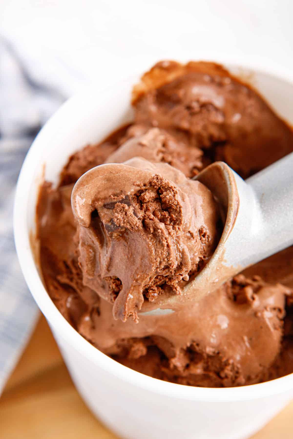 Chocolate ice cream being scooped out of freezer safe container. 