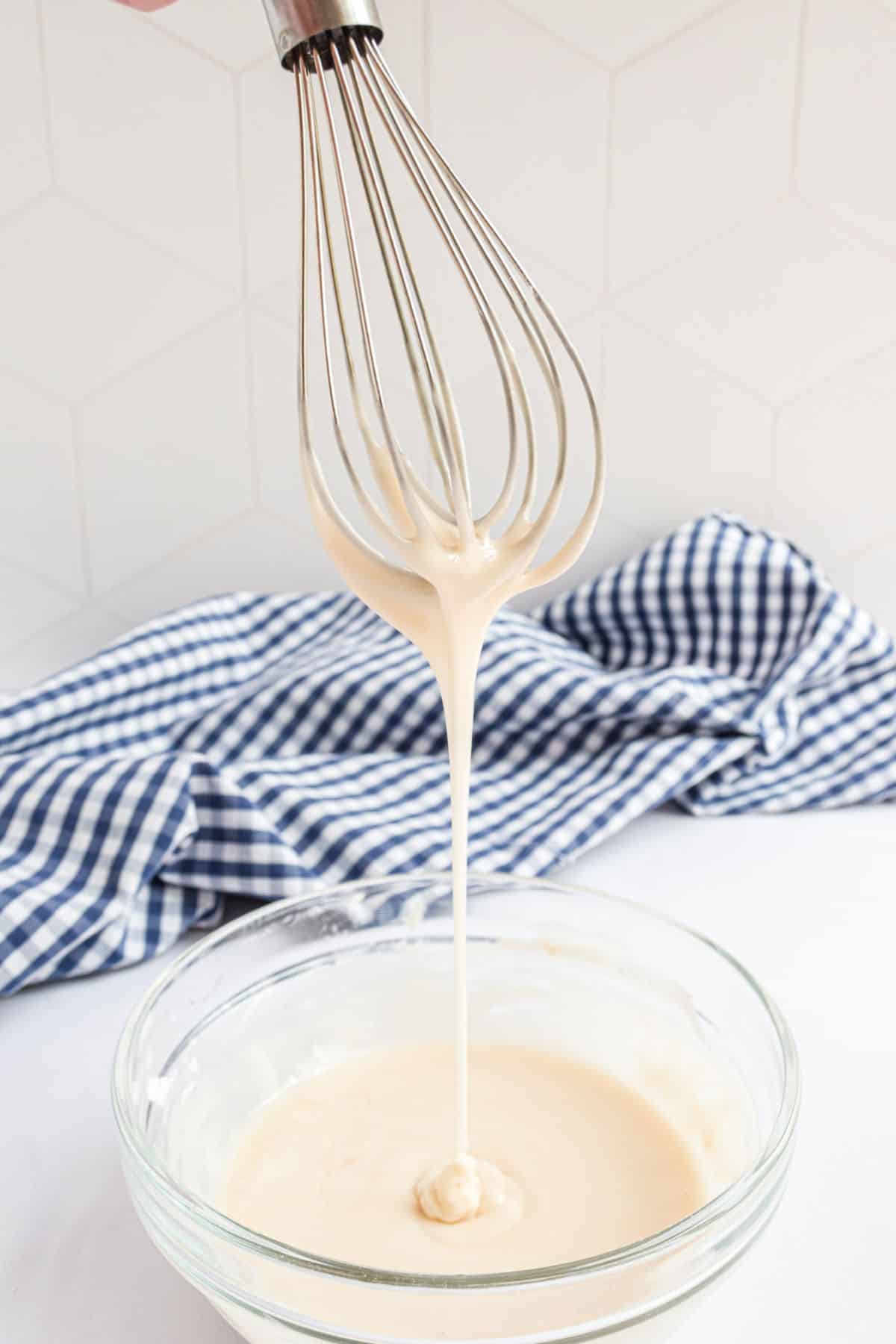 Vanilla icing dripping off a whisk into a bowl.
