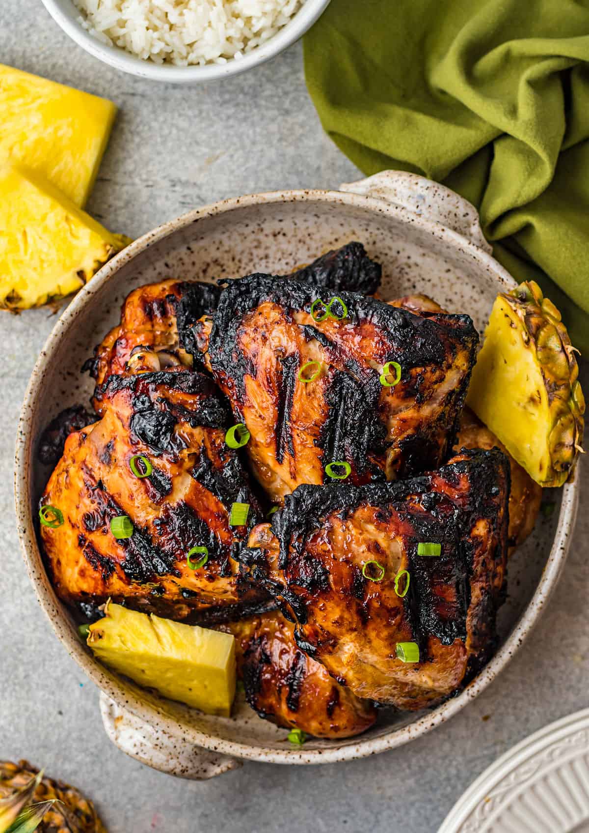 Grilled huli huli chicken in a serving bowl with sliced pineapple.