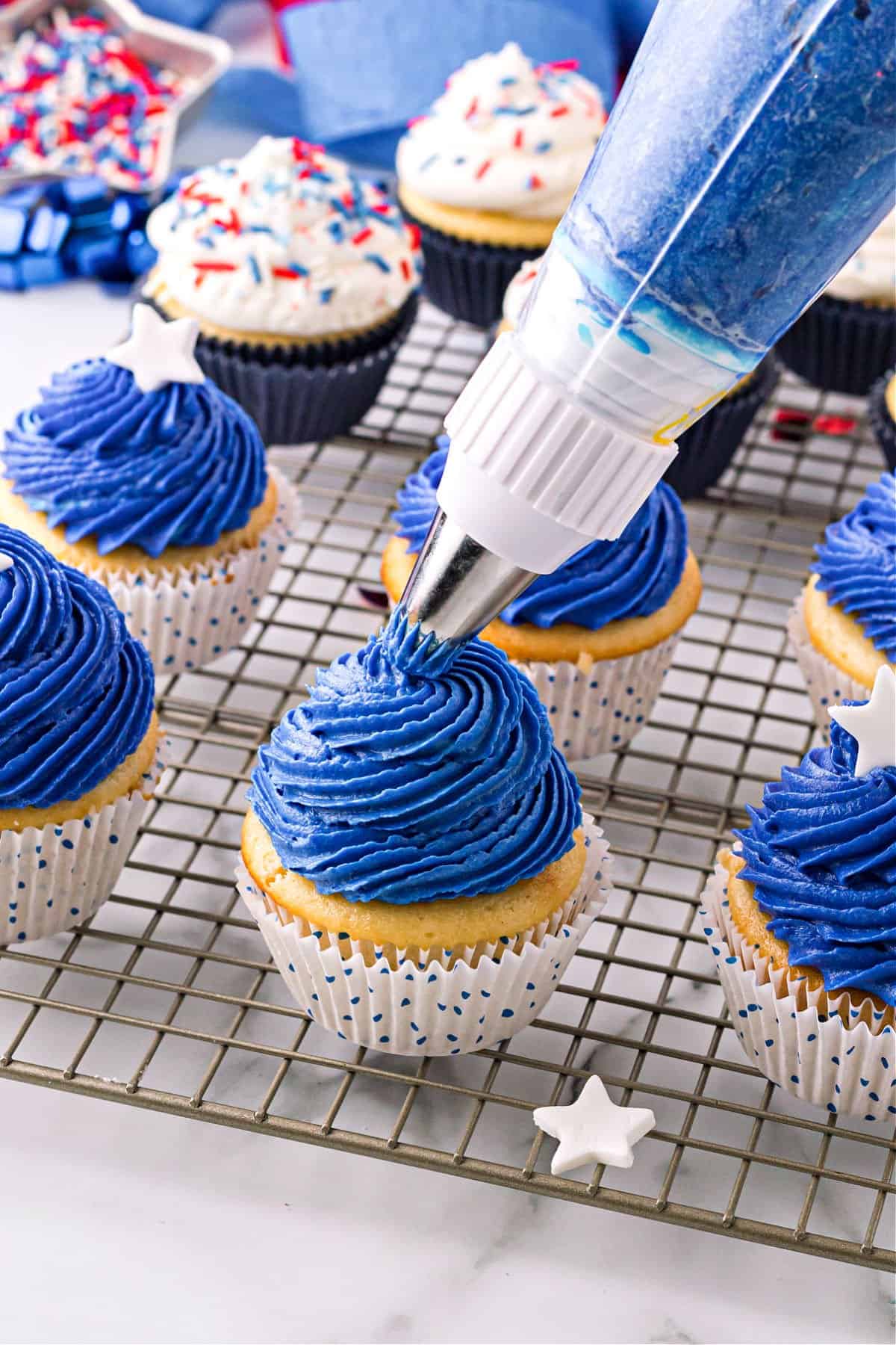 Blue frosting being piped onto vanilla cupcakes.