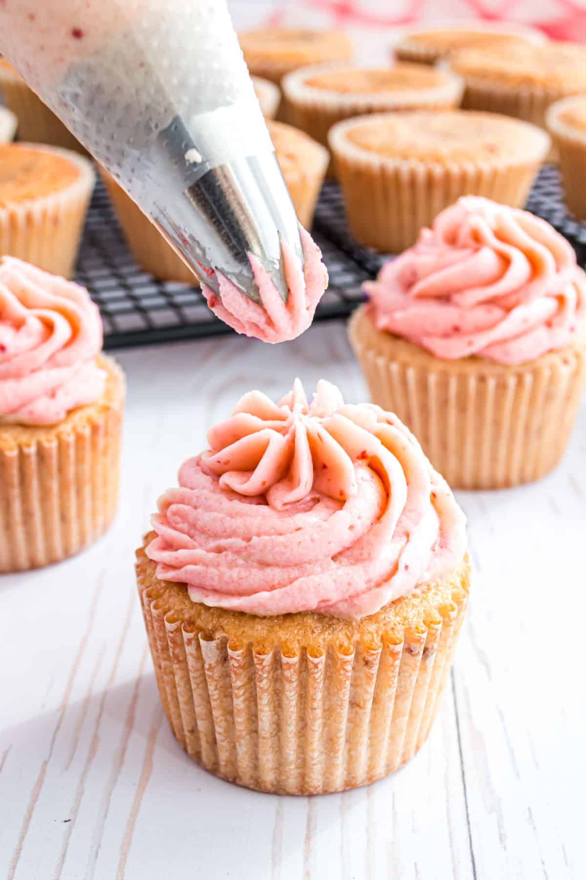 Strawberry cupcakes with strawberry frosting being piped on top.