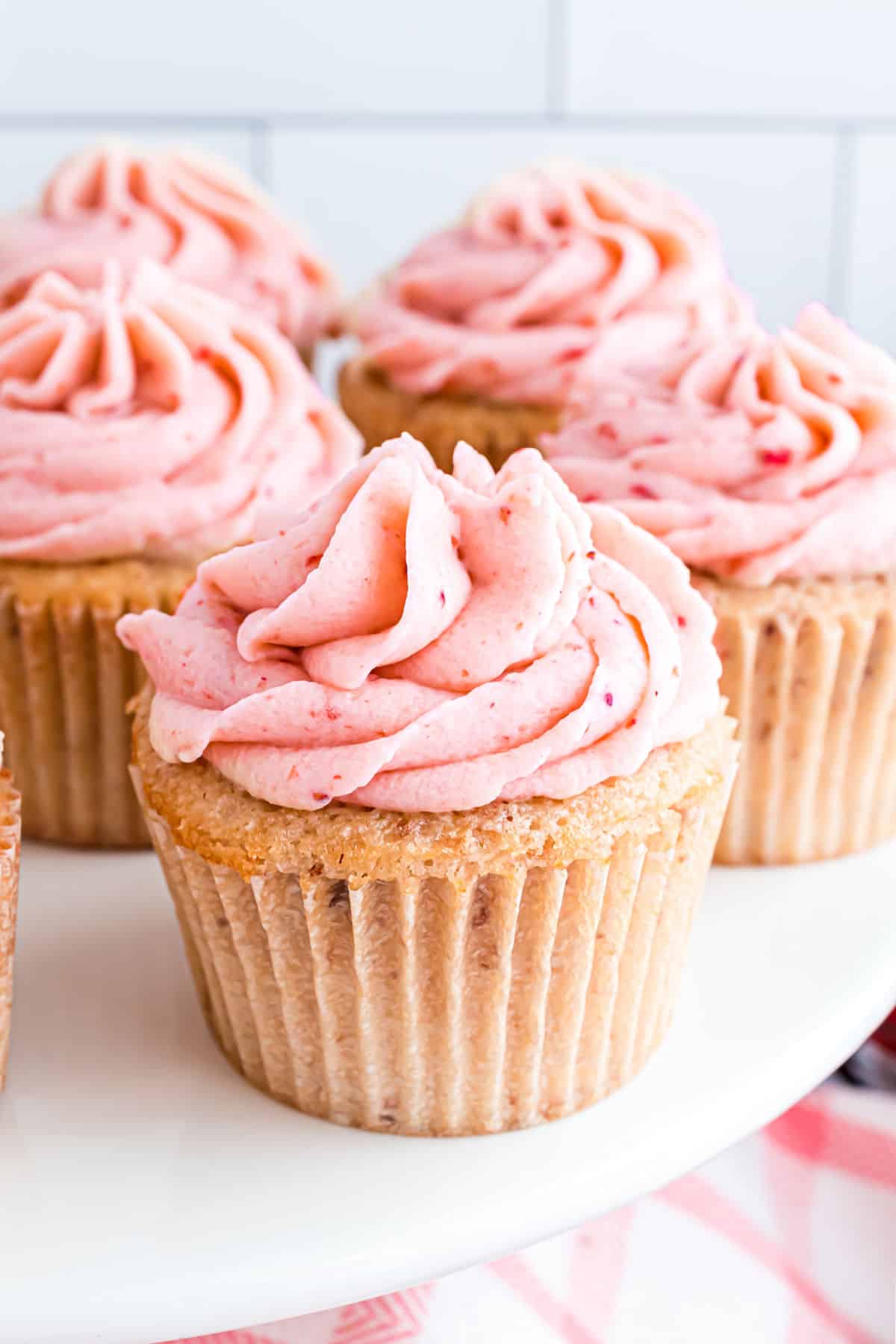 Strawberry cupcakes topped with strawberry frosting on a white cake platter.