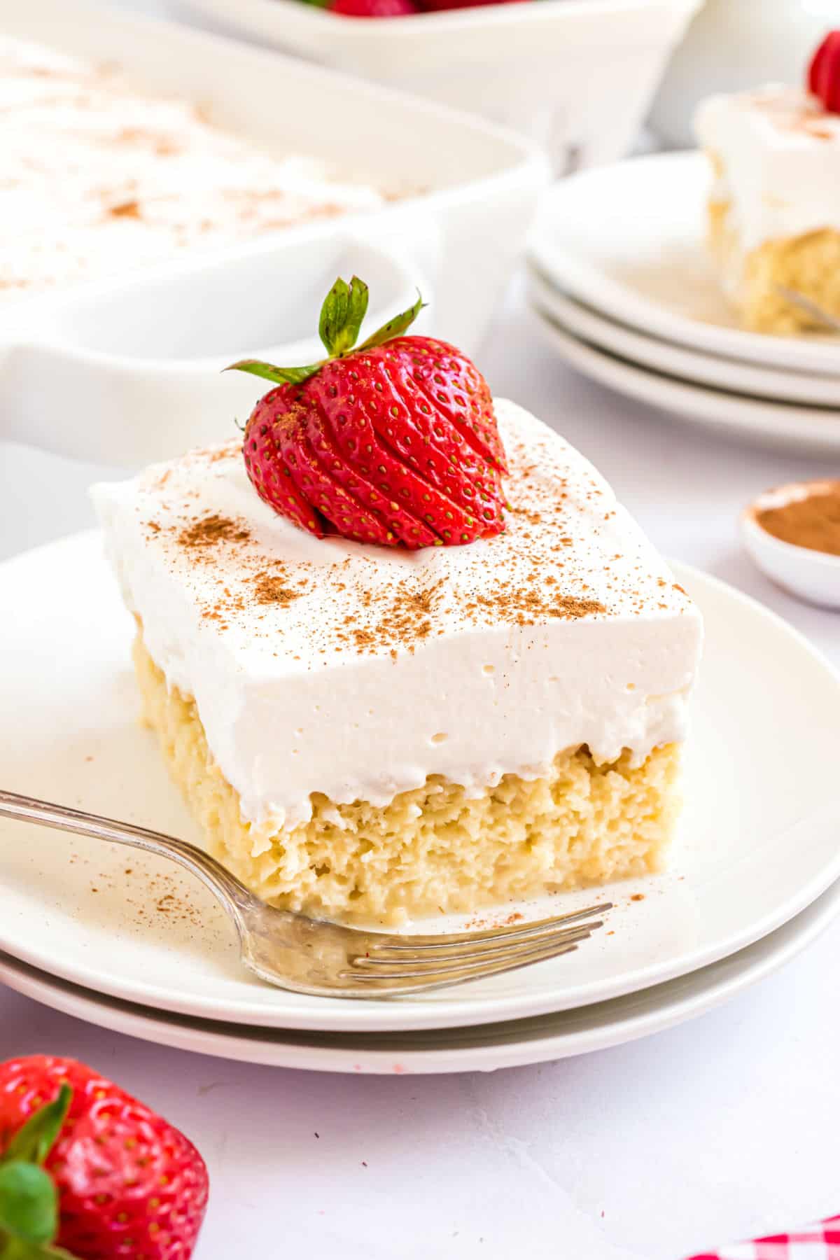 Slice of tres leches cake garnished with a fresh strawberry on a white plate.