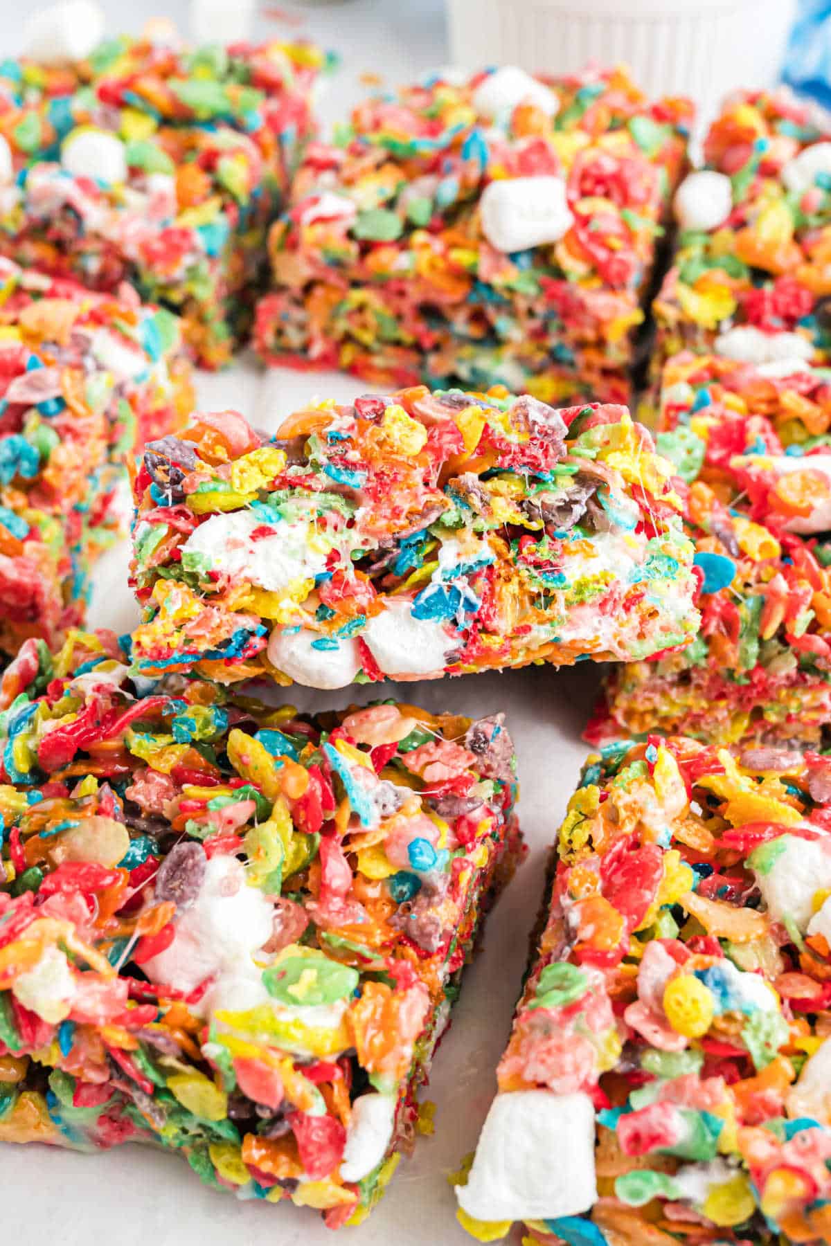 Fruity pebble crispy treats stacked on parchment paper.