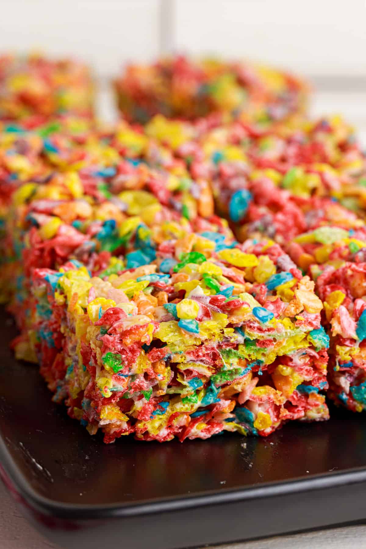 Fruity pebbles marshmallow treats on a black plate.