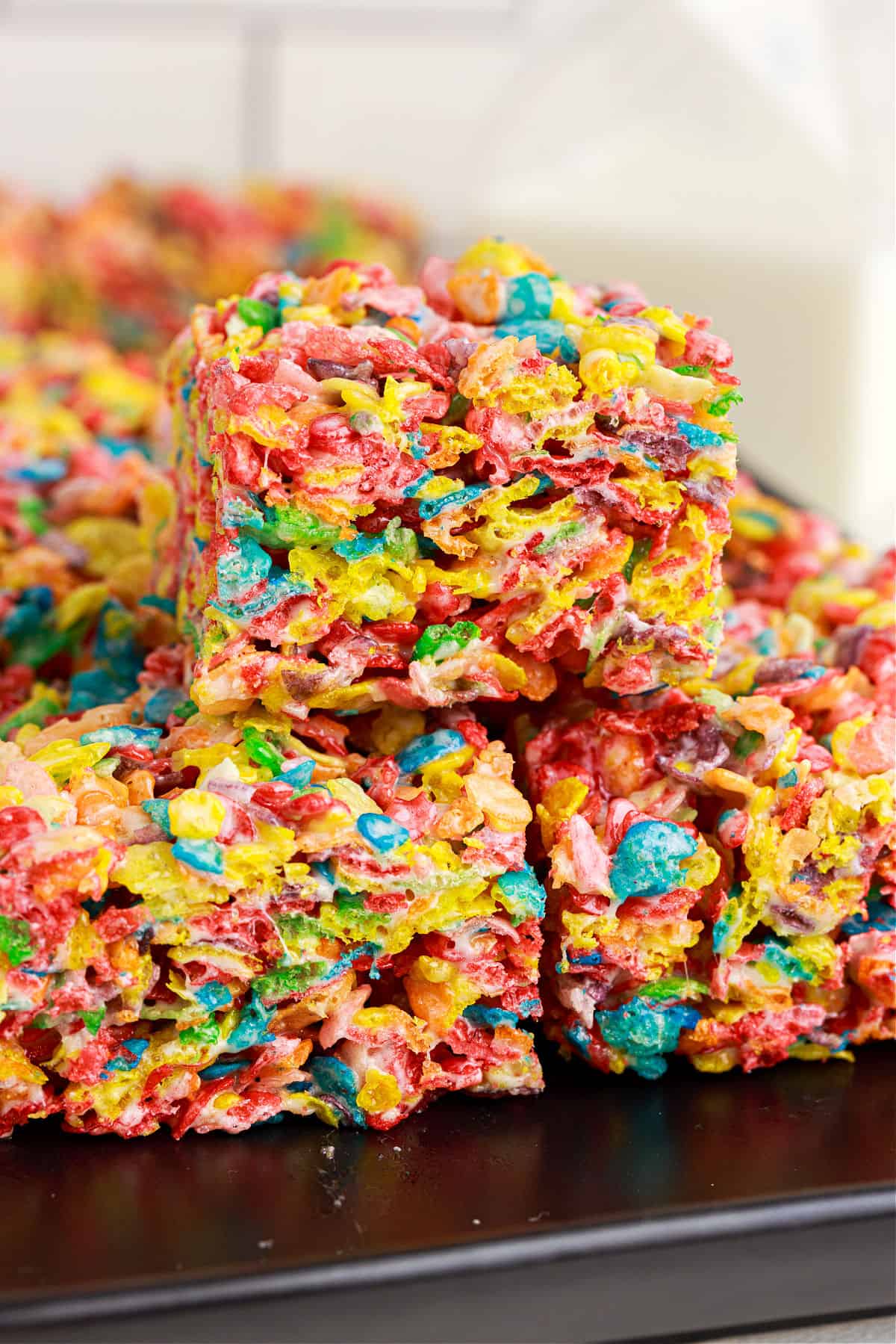 Fruity pebbles cereal treats stacked on a black plate. 