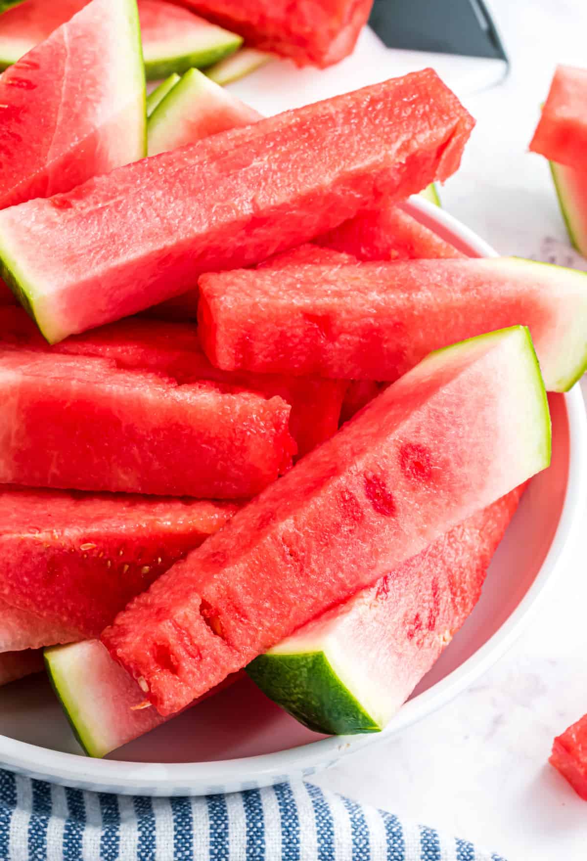 Watermelon cut into sticks with the rinds and served on a white platter.