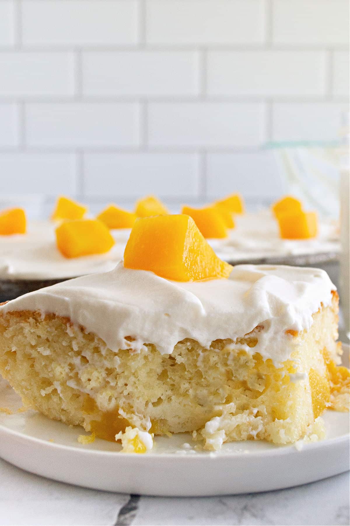 Slice of peach cake with whipped cream on a white dessert plate.