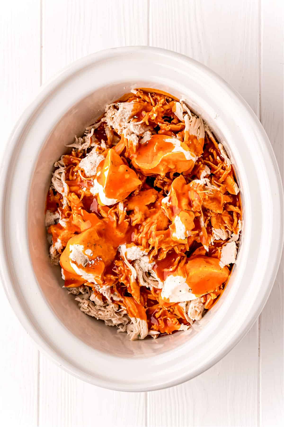 White slow cooker with shredded chicken, wing sauce, and cheeses.