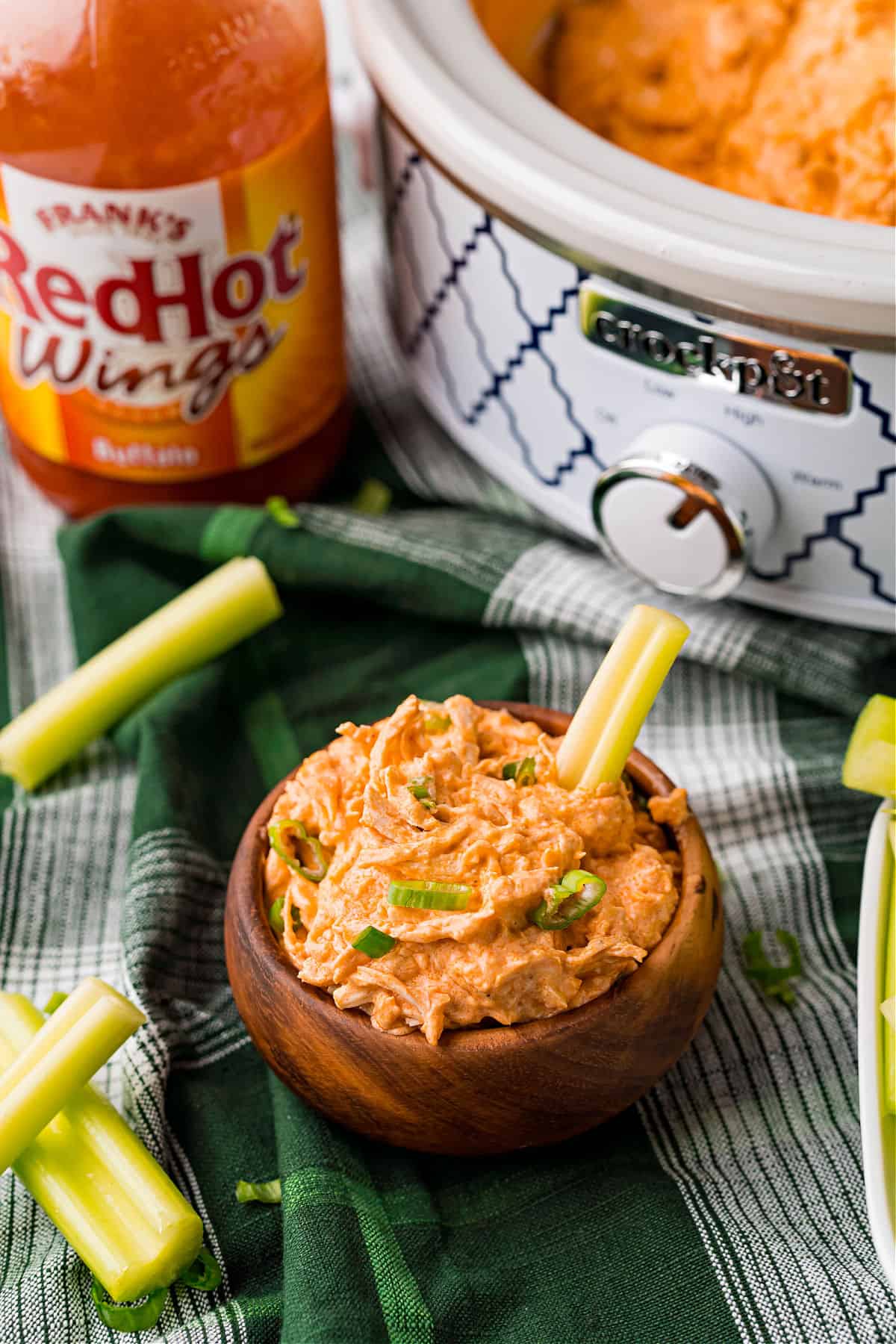 Buffalo chicken dip in a bowl with slow cooker in background.