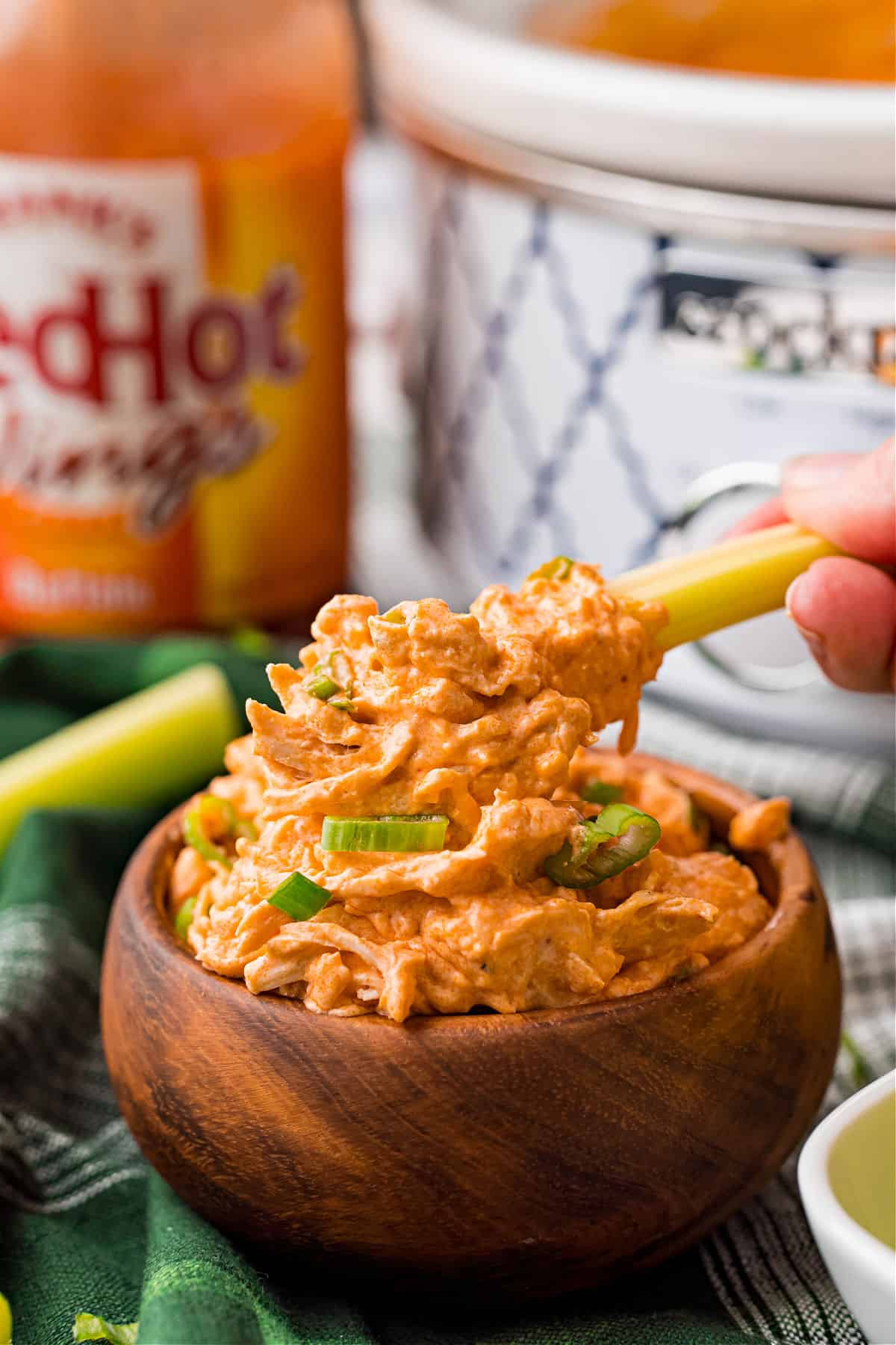 Buffalo chicken dip in a wooden bowl with a celery stick dipper.