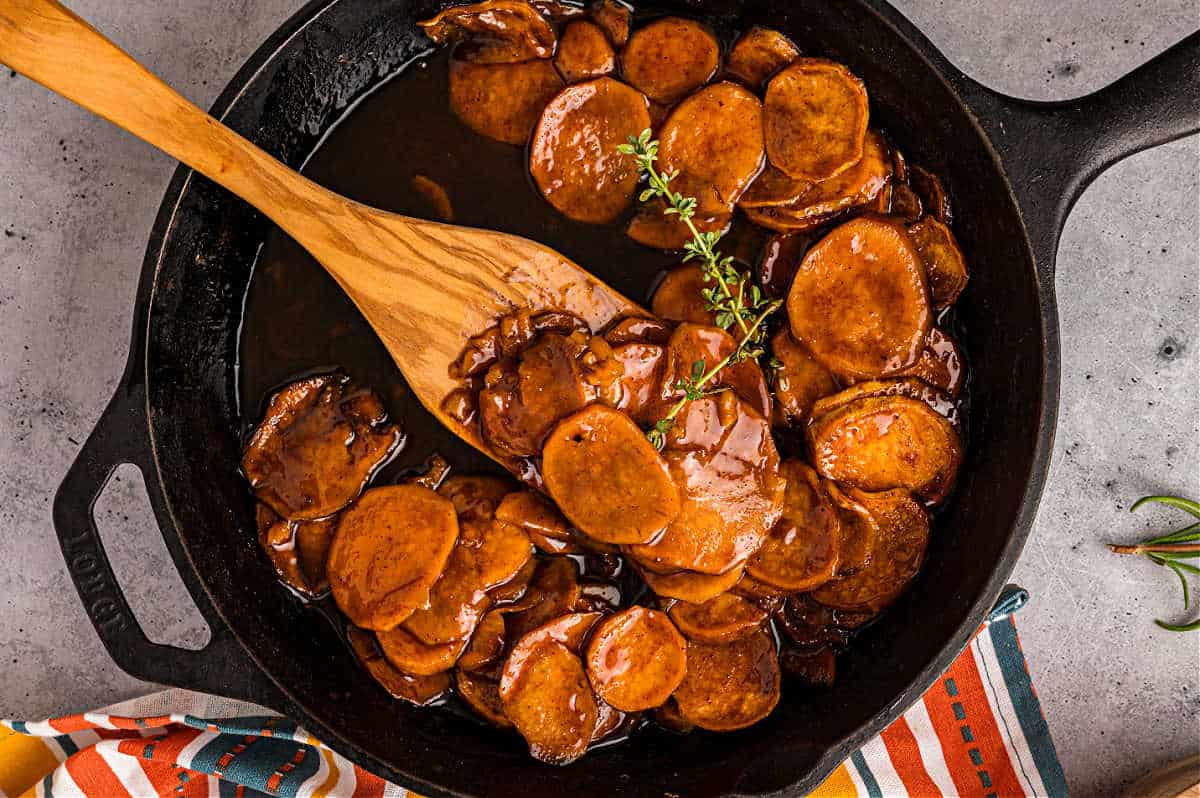 Candied sweet potatoes in a skillet with wooden spoon to serve.