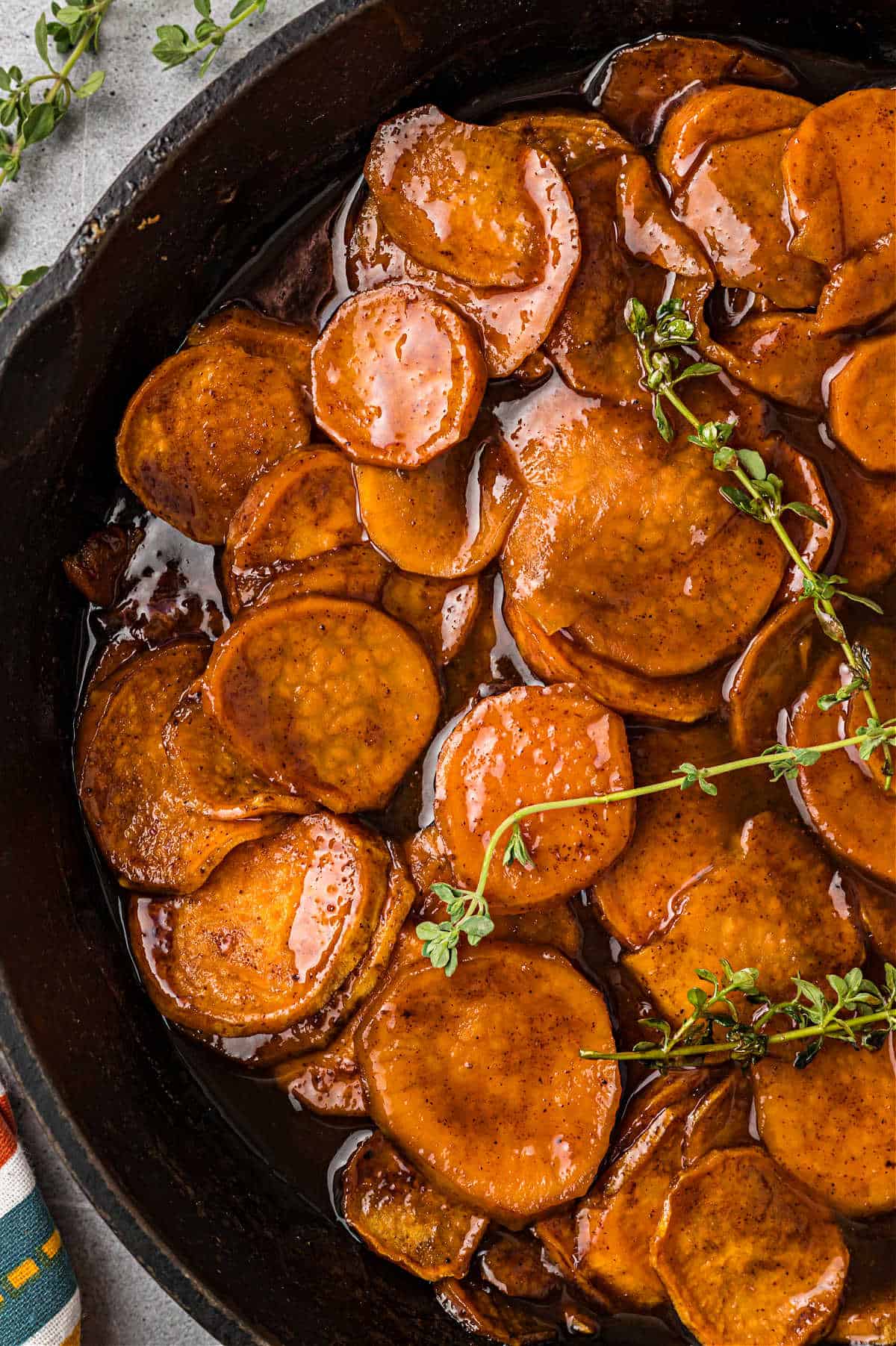 Candied sweet potatoes in a cast iron skillet with fresh thyme.