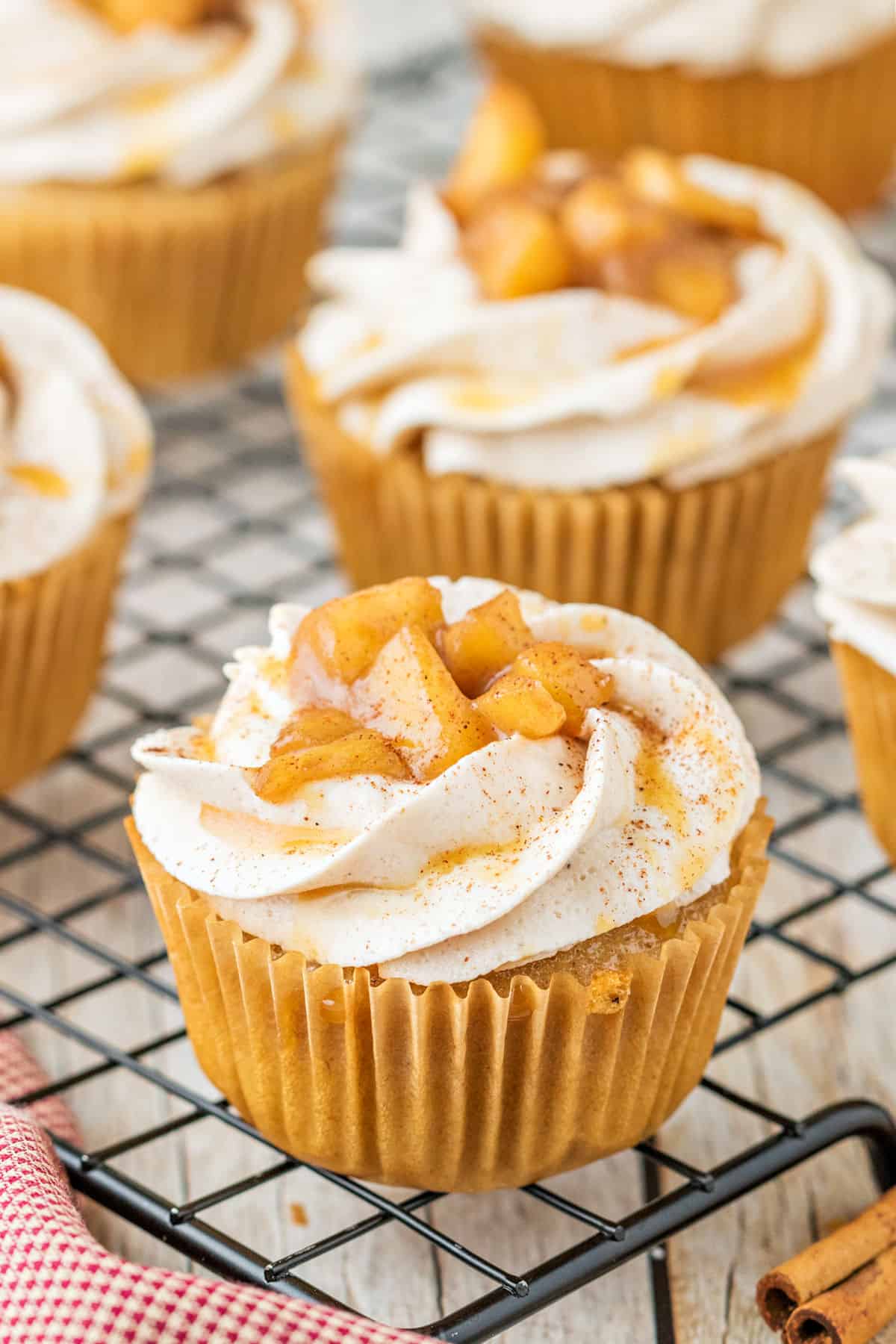 Apple topped cupcakes with frosting on a wire cooling rack.