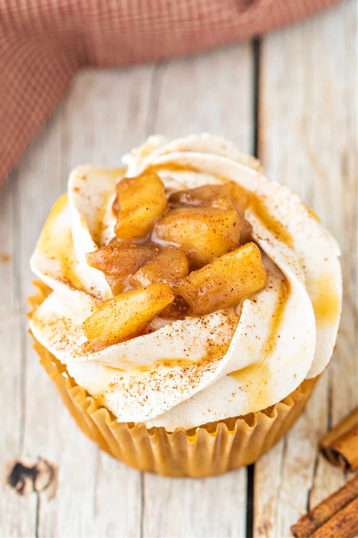 Caramel apple stuffed cupcake with buttercream and caramel sauce on wooden counter.