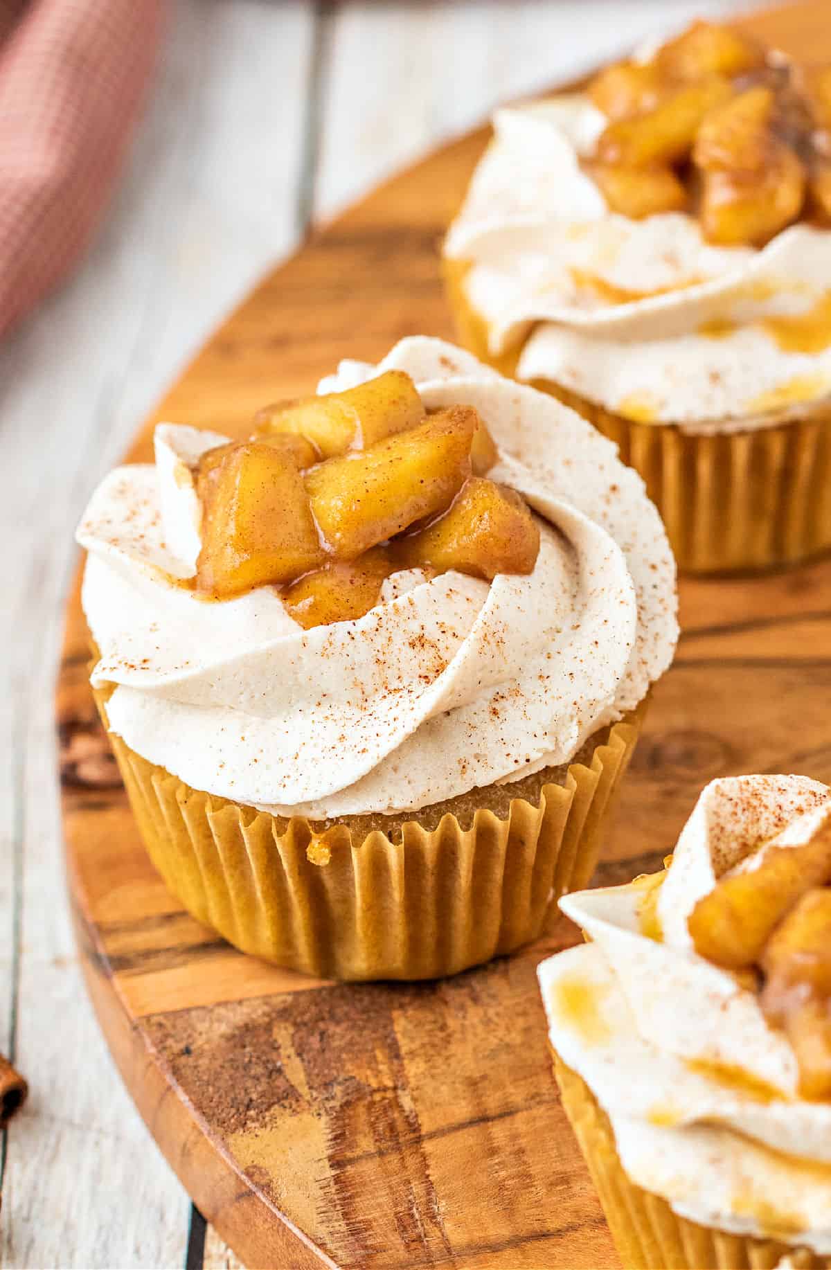 Apple cupcakes with frosting and caramel apple topping on a wooden serving tray.