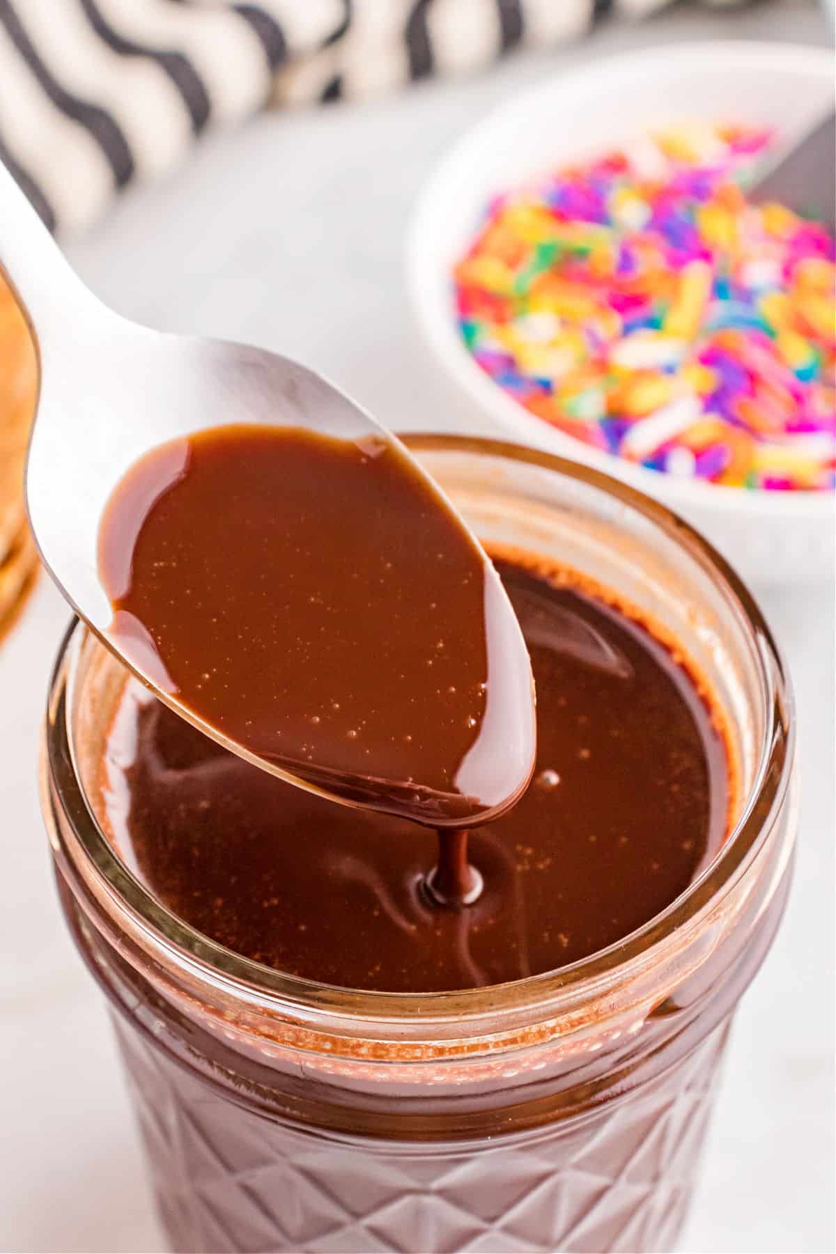 Homemade chocolate syrup in a jar with a spoon.