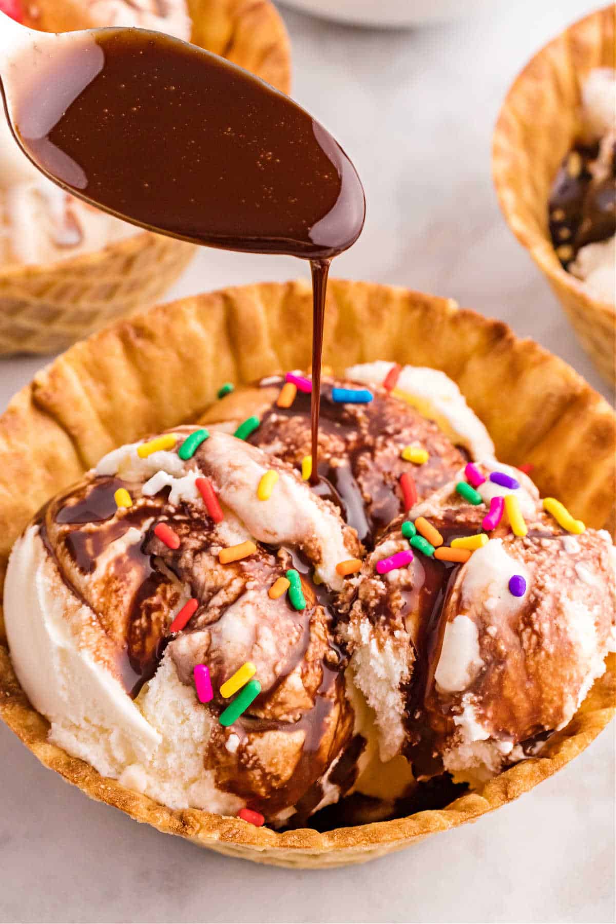 Chocolate syrup being drizzled over a waffle bowl of vanilla ice cream.