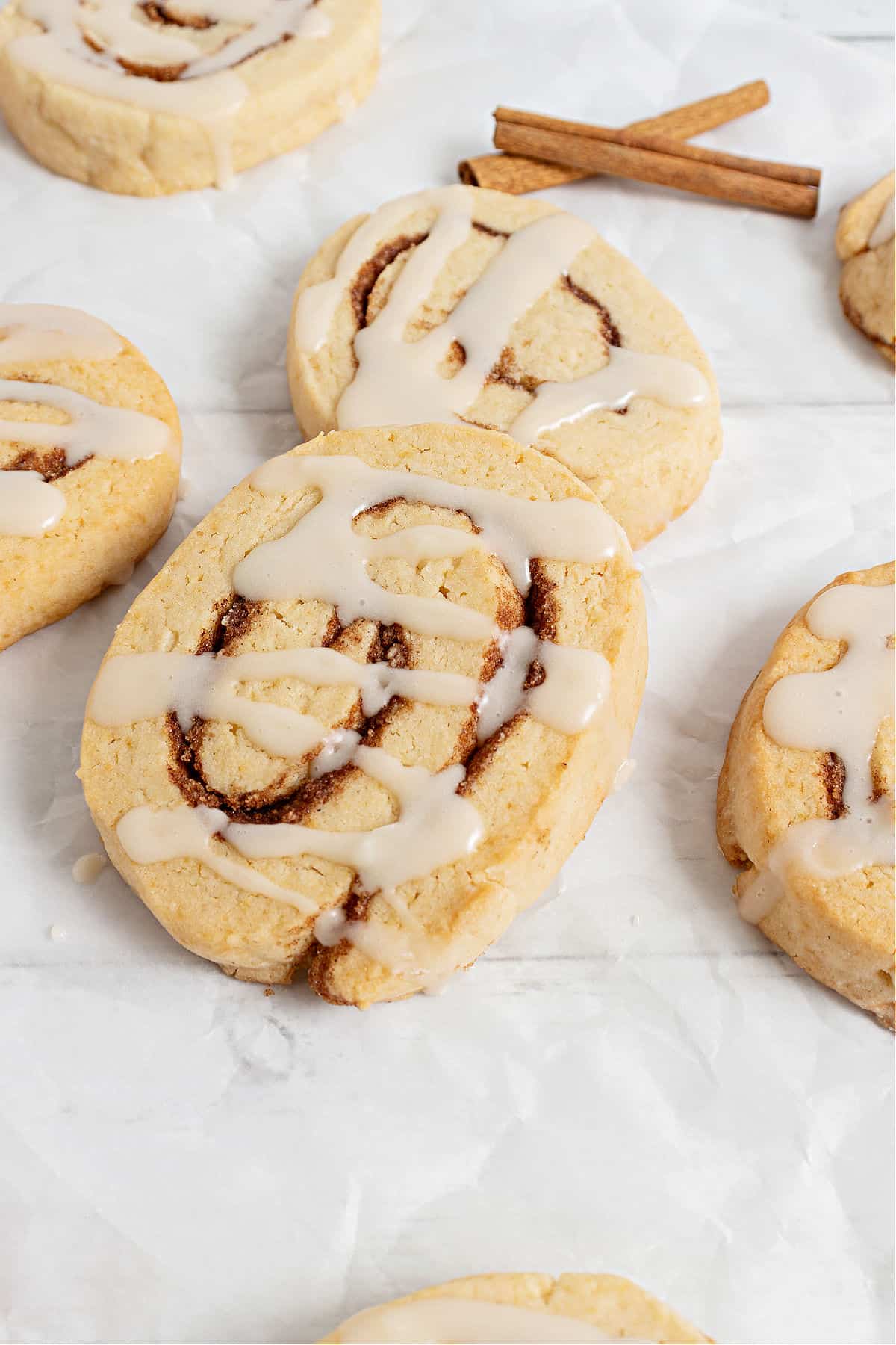Cinnamon roll cookies drizzled with cream cheese icing on a piece of parchment paper.